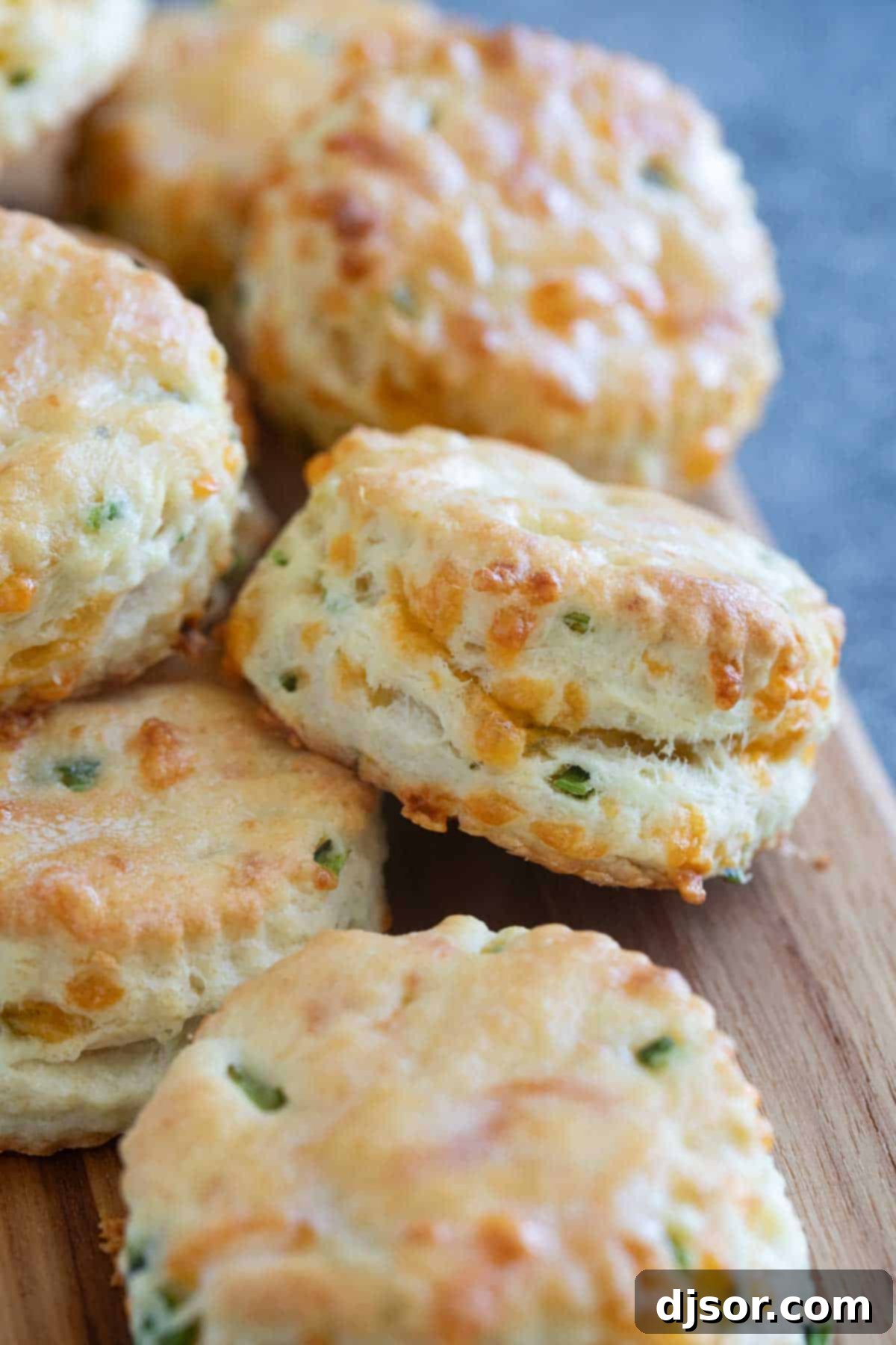 A stack of golden brown Jalapeno Cheddar Biscuits on a cutting board, showcasing their flaky texture.
