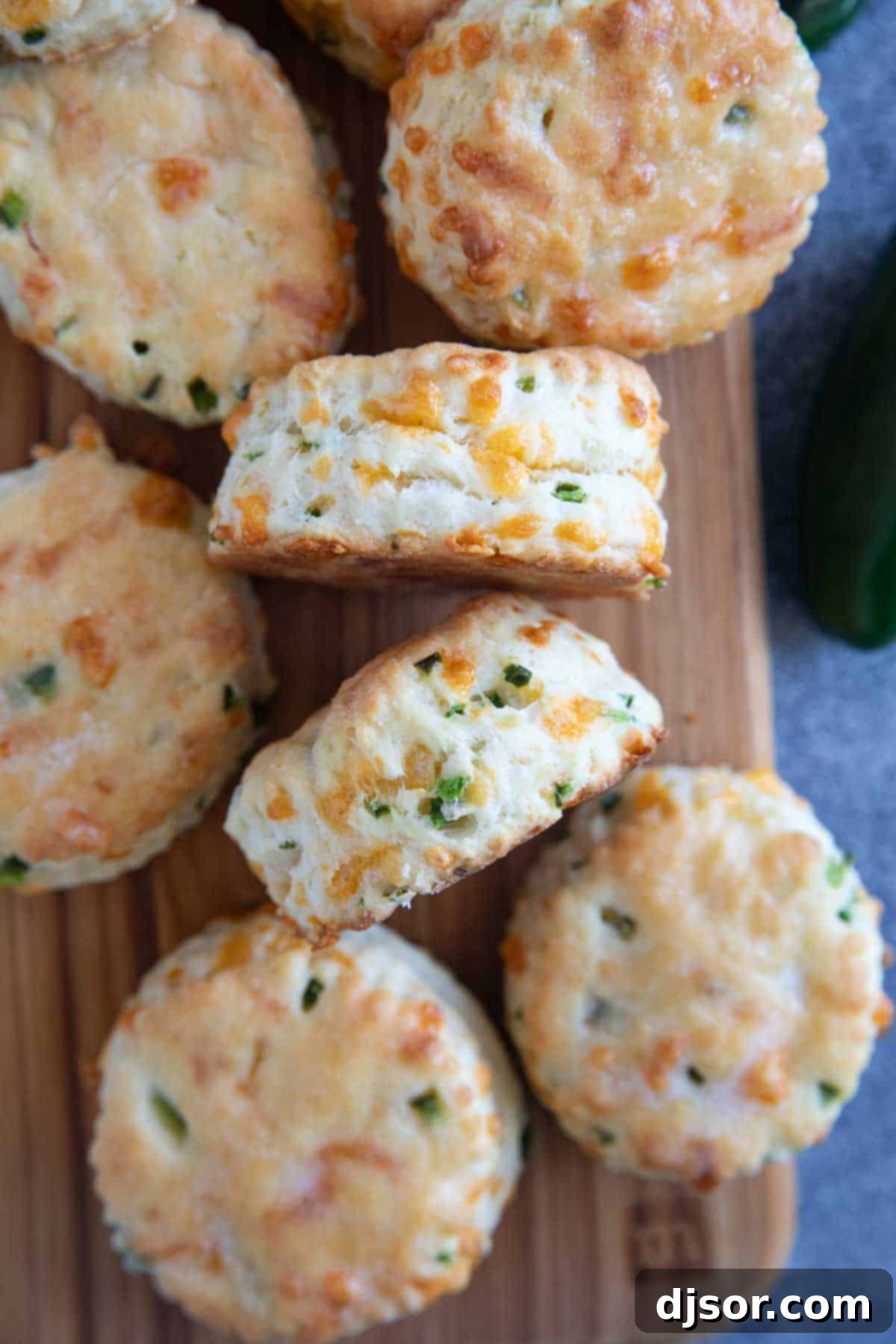 Jalapeño cheddar biscuits stacked on a cutting board, with two biscuits turned on their sides to show their layered texture.
