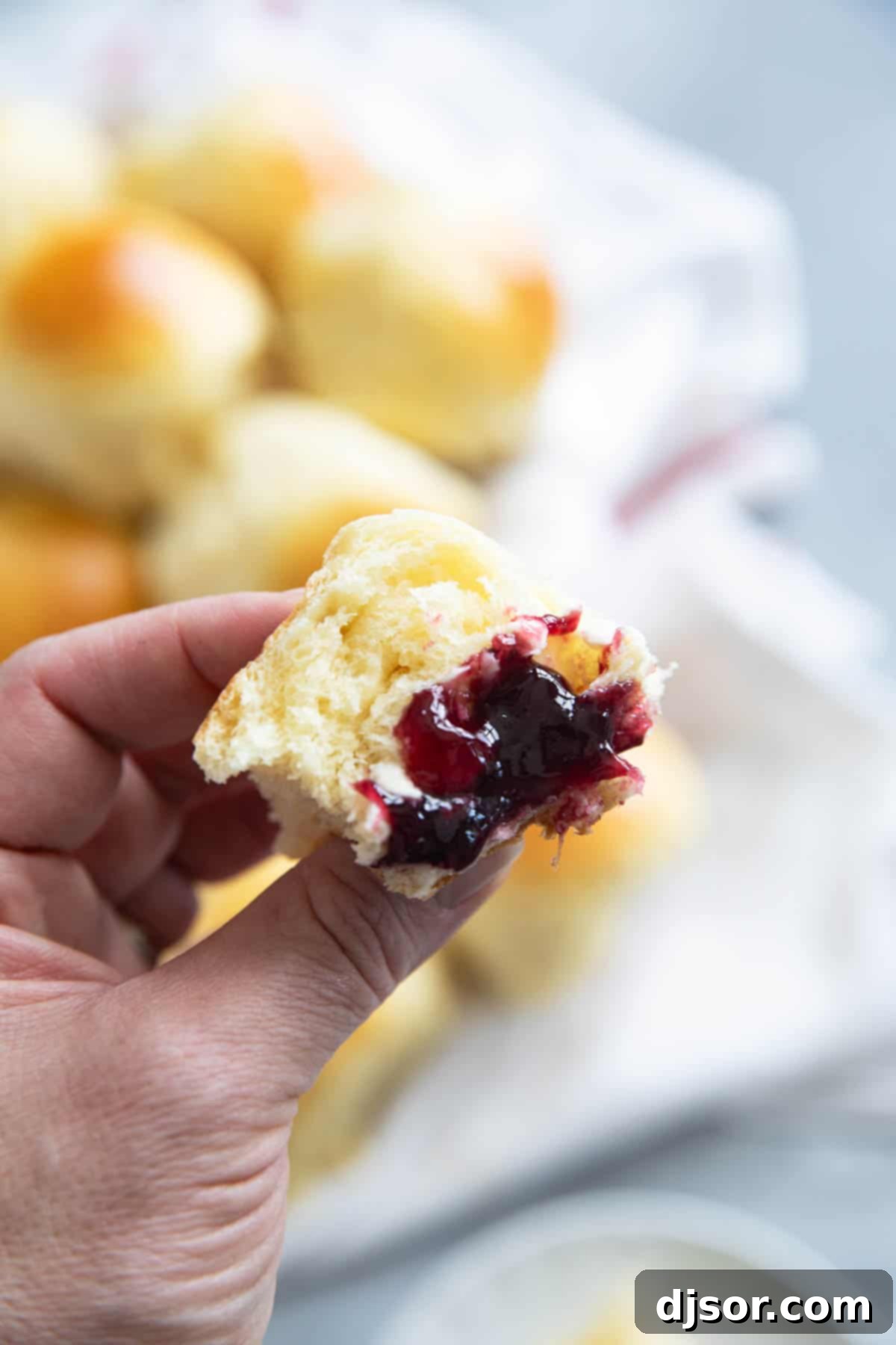 A hand holding a Brioche Roll, gently torn, showing its soft interior, served with jam and butter.