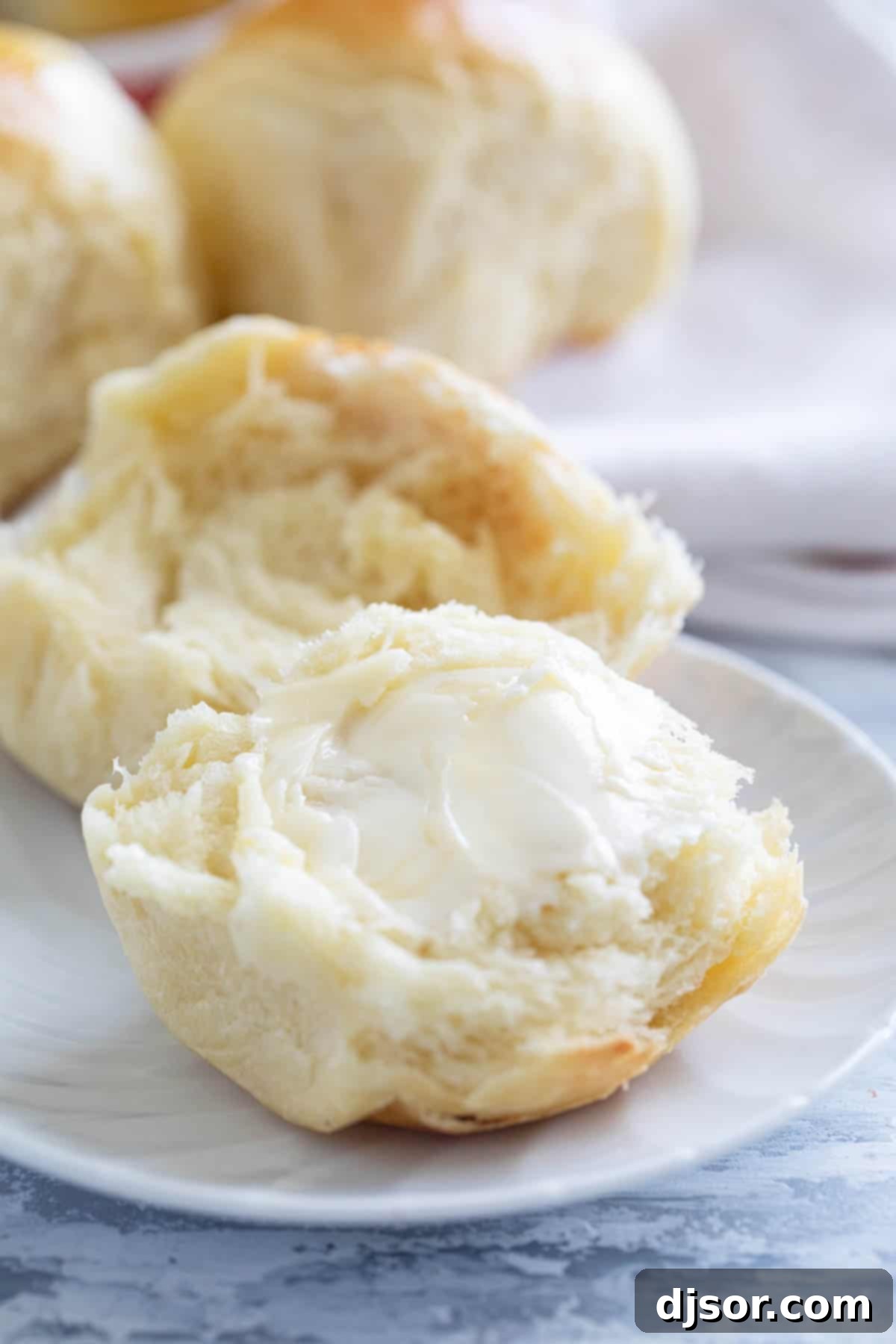 A Brioche Roll torn in half, revealing its tender crumb, topped with a pat of butter.