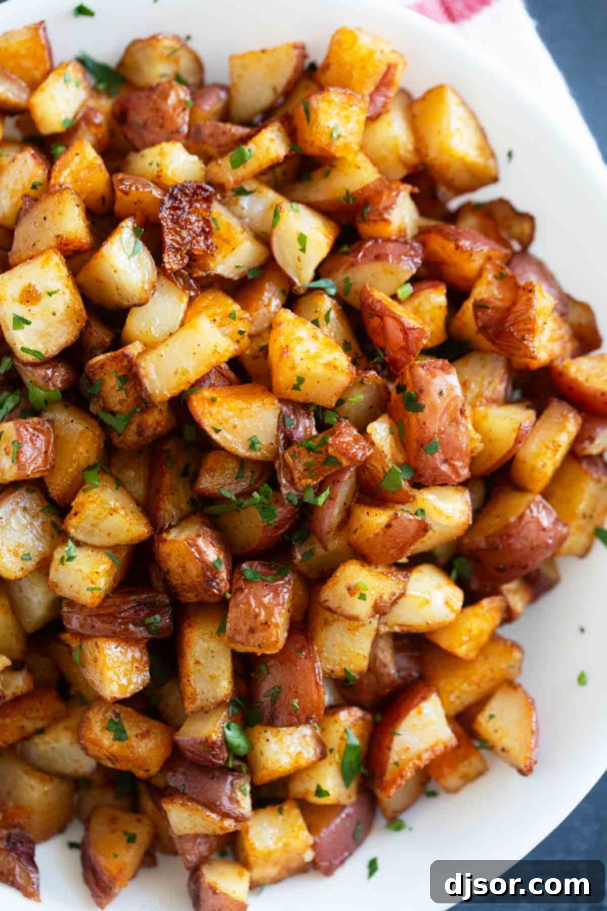 Oven roasted Breakfast Potatoes with a golden crispy exterior, sprinkled with fresh parsley on a serving plate, ready to be enjoyed.