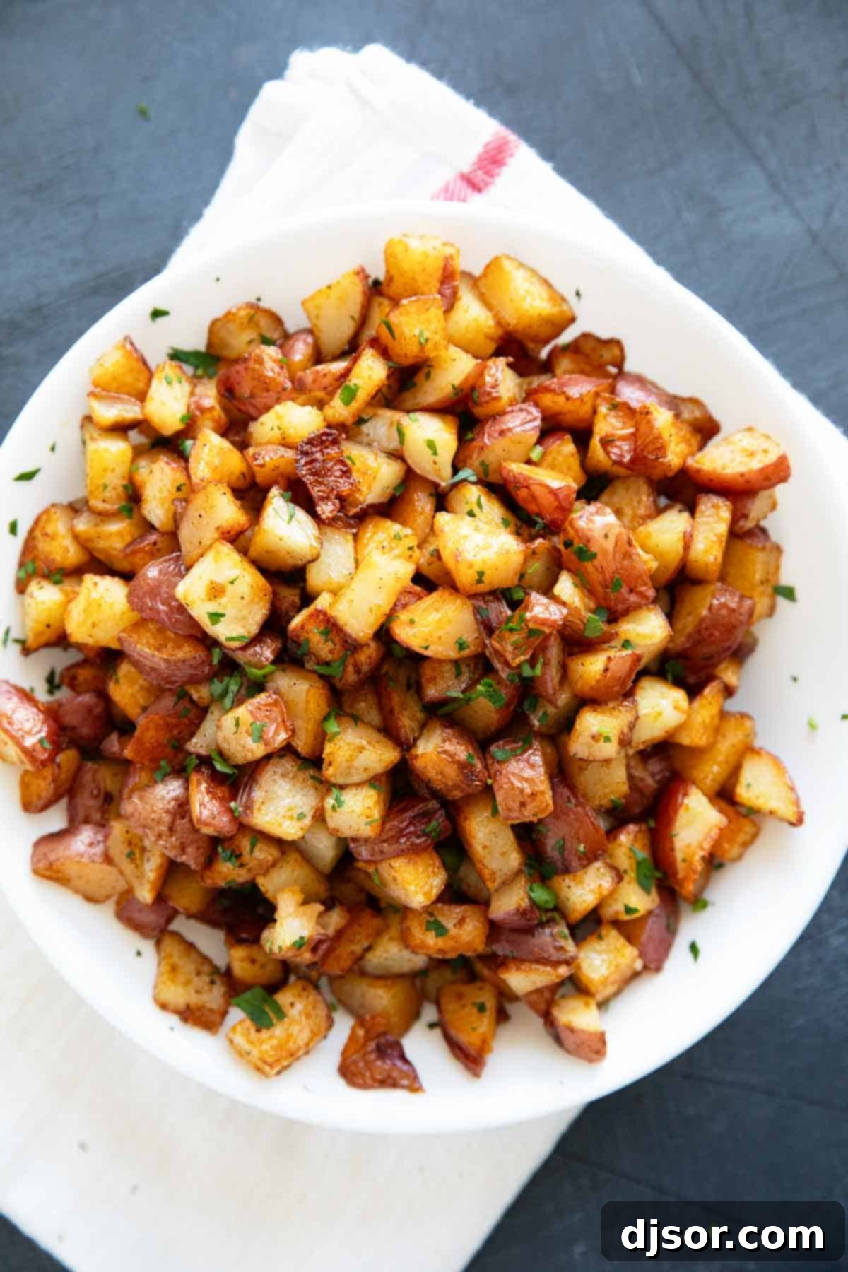 A beautiful wooden plate piled high with golden-brown, crispy oven-roasted breakfast potatoes, ready to be enjoyed as a hearty morning meal.