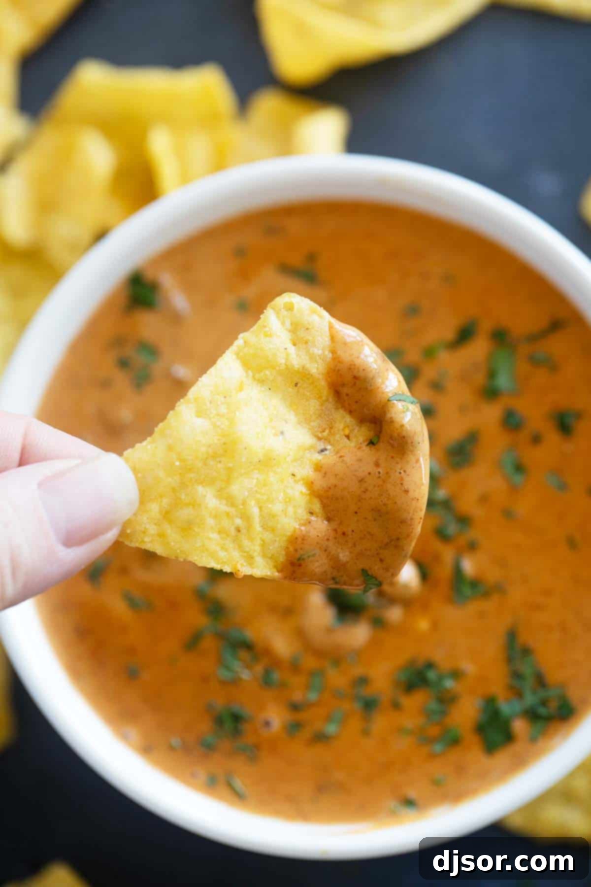 Chip with Chili's Queso Dip on it, over a bowl of queso.