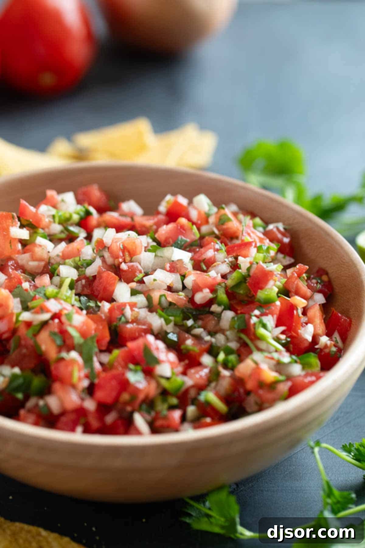 A large wooden bowl filled to the brim with freshly made Pico de Gallo, showcasing its vibrant red, white, and green colors, ready to be served.