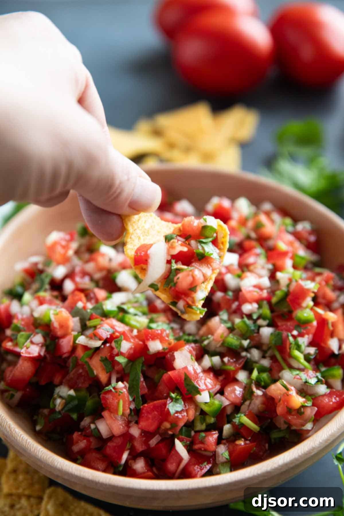 A hand dipping a crispy tortilla chip into a bowl of fresh Pico de Gallo, highlighting the vibrant colors and chunky texture of the salsa.