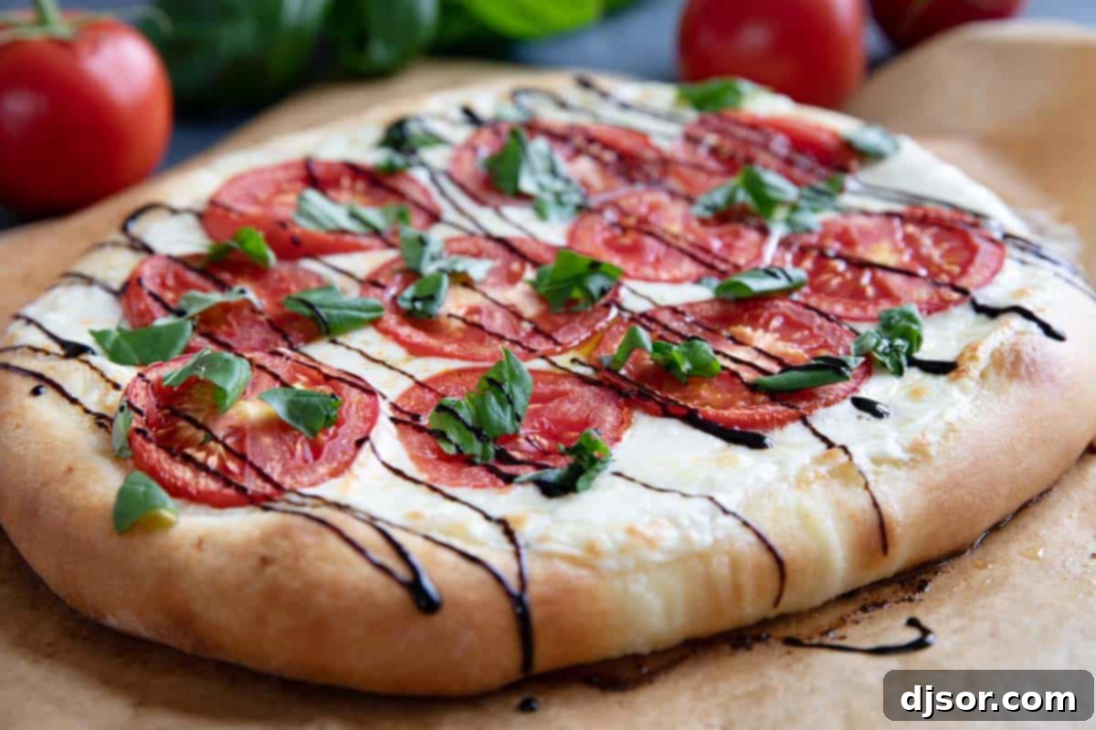 Caprese Pizza topped with fresh tomatoes and balsamic glaze with extra ingredients in the background.