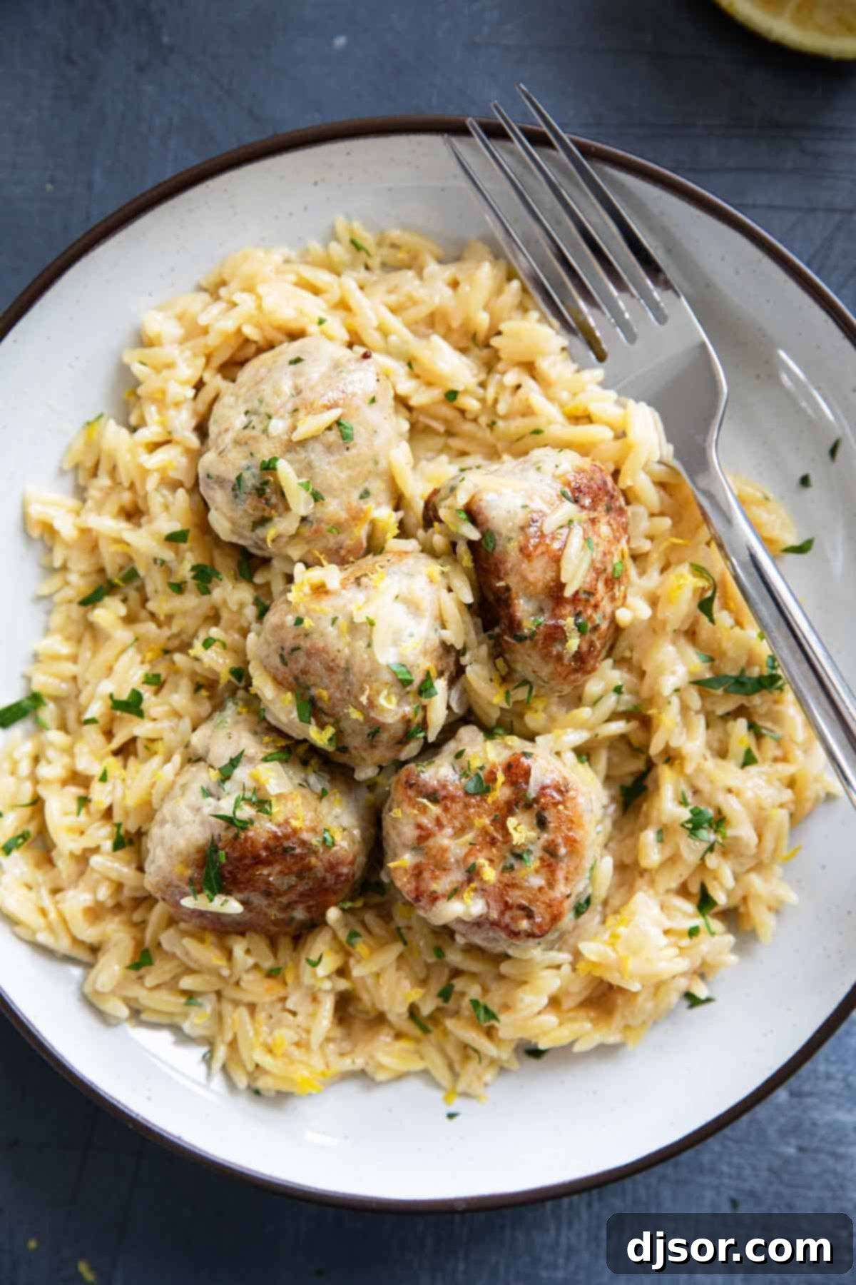 A generously portioned plate showcasing tender chicken meatballs elegantly arranged over a bed of creamy, bright lemon orzo, ready to be enjoyed. This image captures the delicious appeal of the finished one-pan meal.