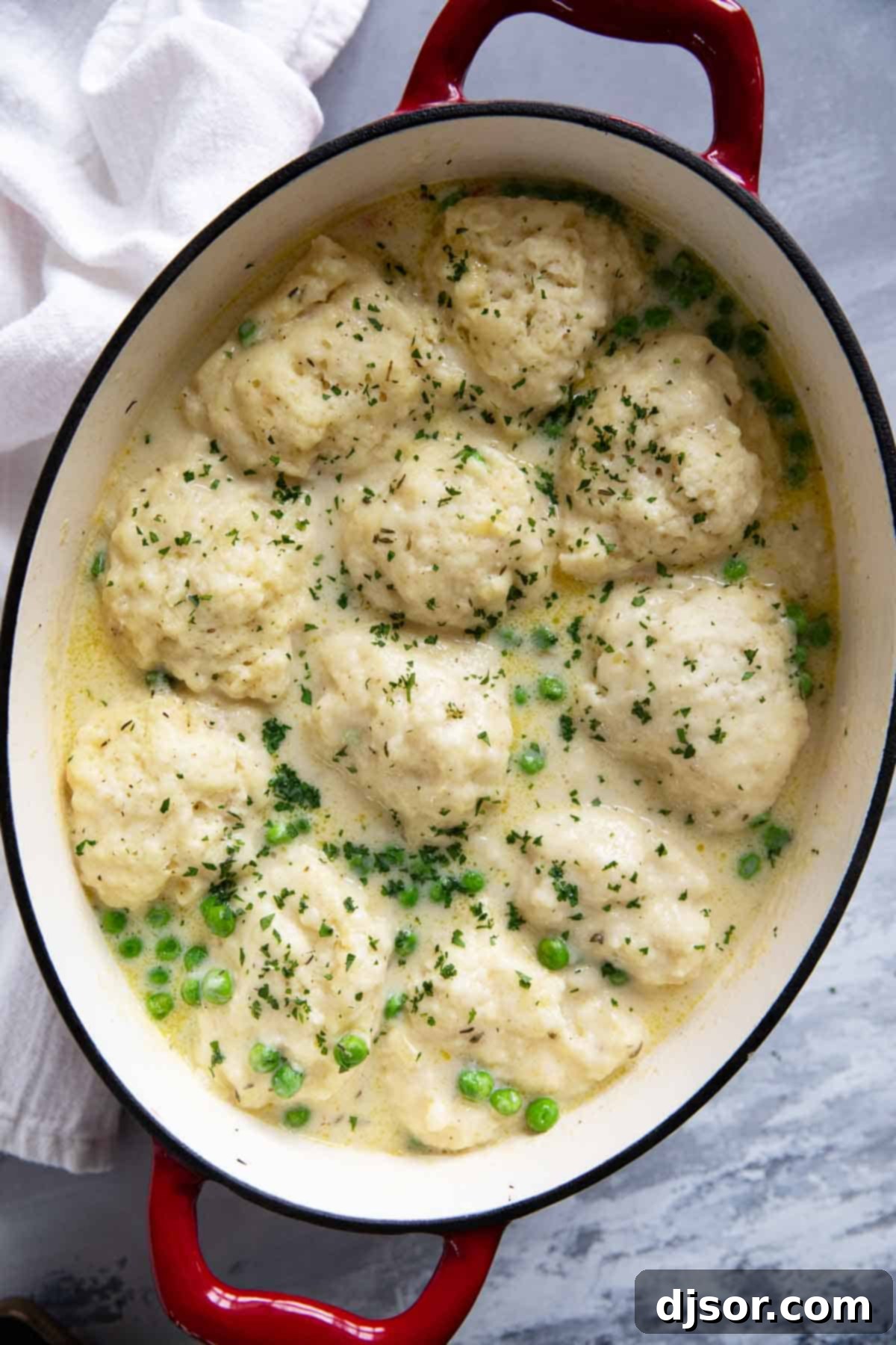 A close-up shot of a large soup pot filled with perfectly cooked chicken and dumplings, garnished generously with fresh green herbs. Steam rises, emphasizing the warmth and inviting nature of the dish.