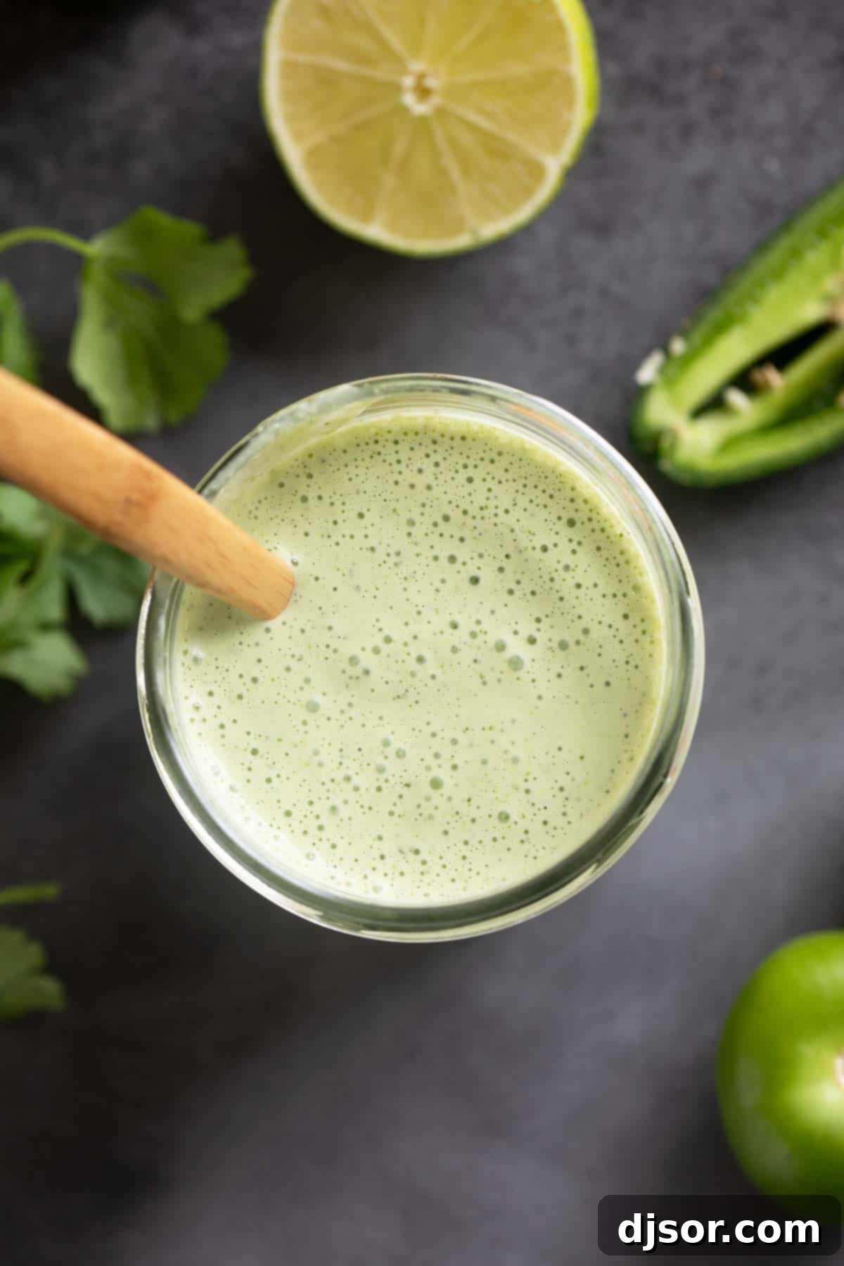 Tomatillo Ranch Dressing in a glass jar, artfully arranged with fresh tomatillos, cilantro, limes, and a vibrant jalapeño pepper for a picturesque display.