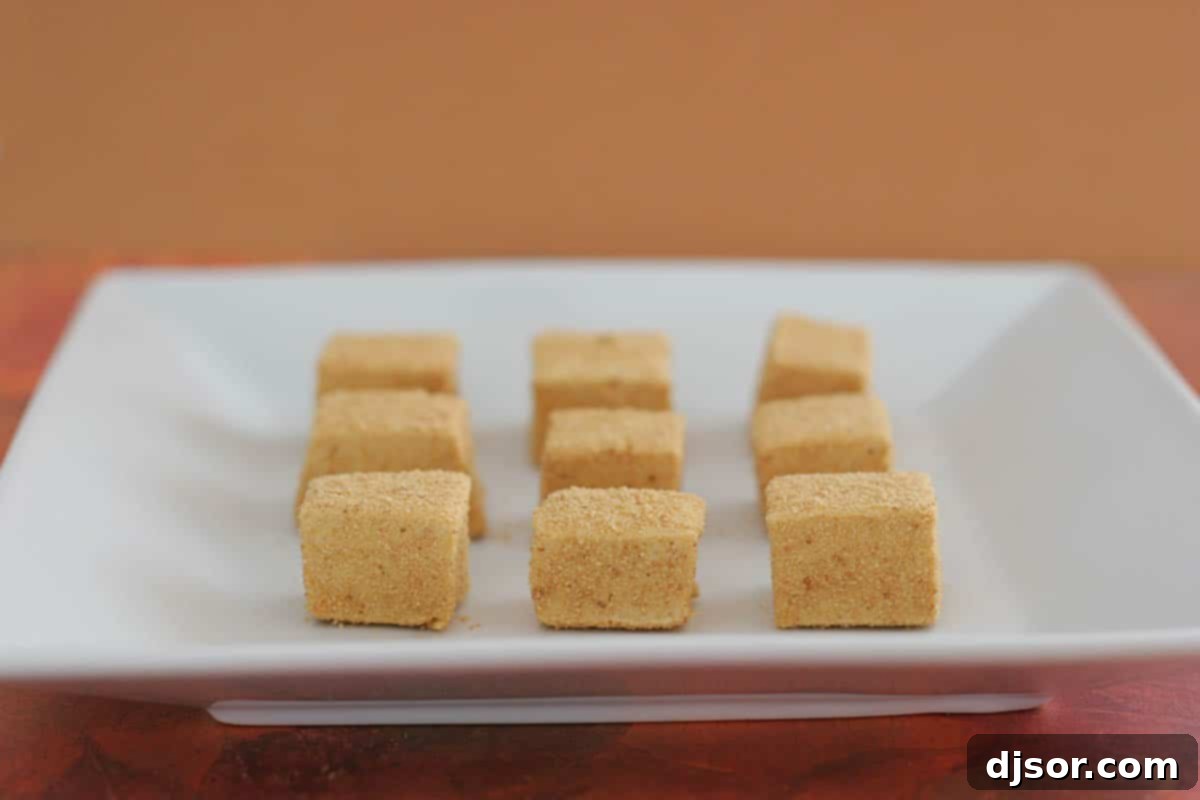 Delectable Homemade Pumpkin Spice Marshmallows for Fall Treats Nine perfectly cubed pumpkin spice marshmallows resting on a pristine white plate, showcasing their inviting orange hue and light coating.