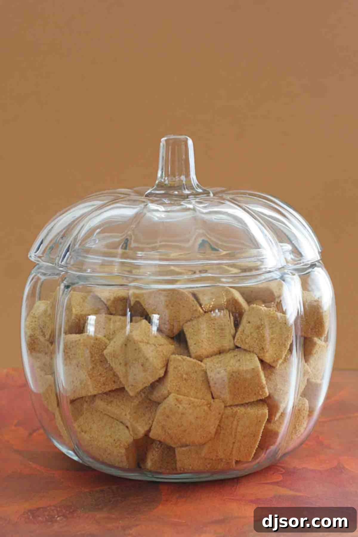 Festive Pumpkin Spice Marshmallows for Fall Gatherings A charming glass pumpkin-shaped bowl overflowing with fluffy, square-cut Pumpkin Spice Marshmallows, invitingly presented.
