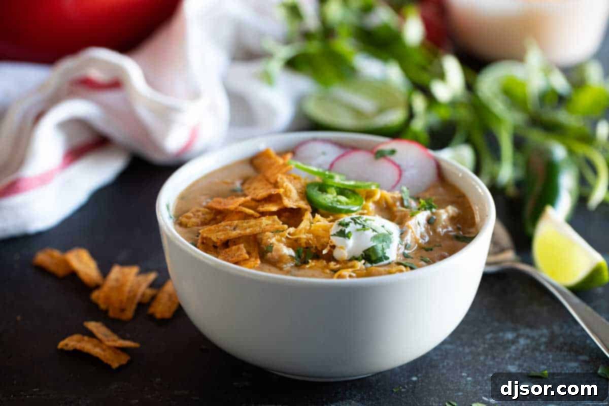 A vibrant bowl of creamy chicken enchilada soup, generously topped with fresh sour cream, crispy tortilla strips, and thinly sliced jalapeños, presented on a rustic wooden surface.