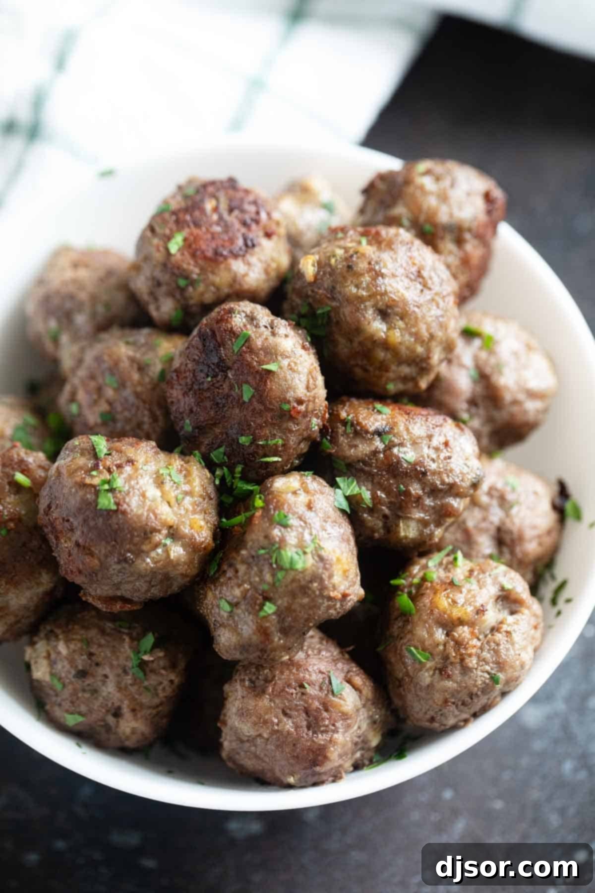 Savory Baked Meatballs 2 Baked meatballs in a bowl sprinkled with parsley. The perfect comforting meal for any occasion, ready to be sauced and served.