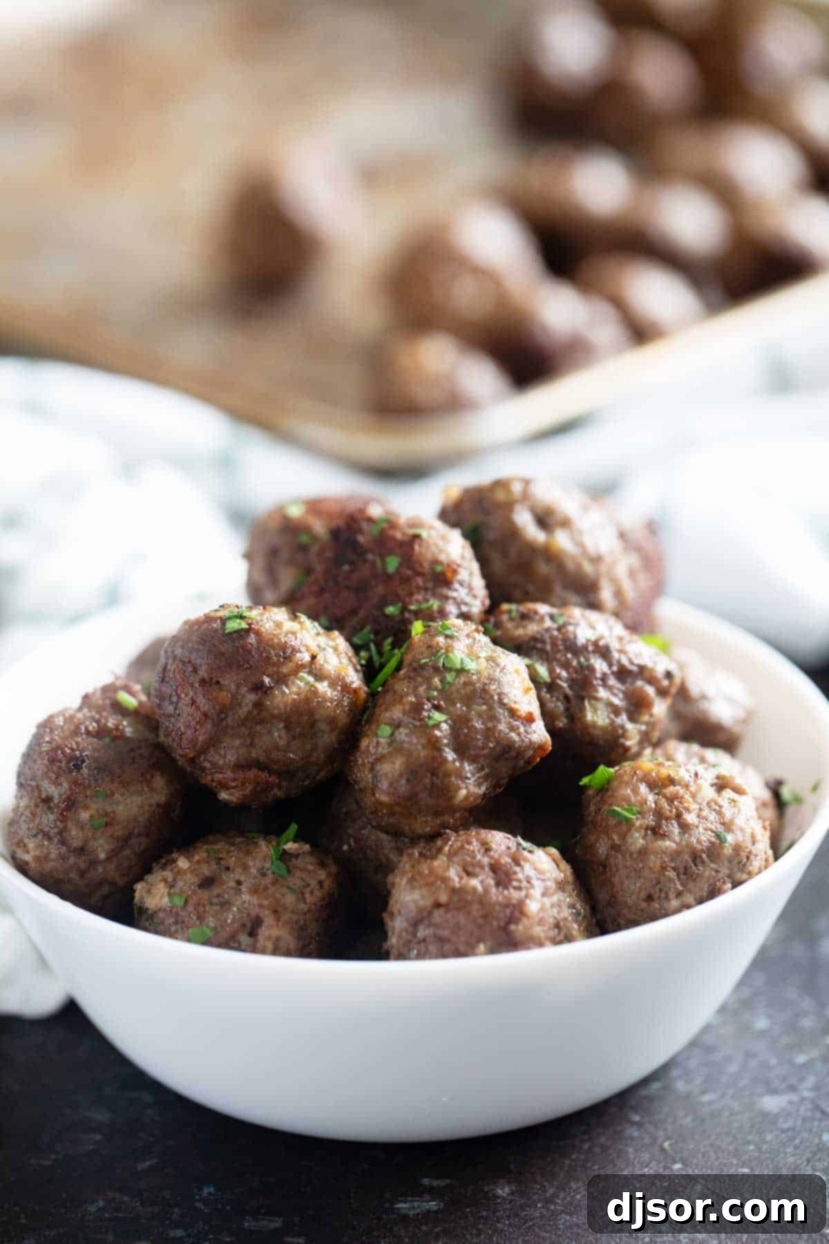 Savory Baked Meatballs 6 A large ceramic bowl overflowing with golden-brown baked meatballs, garnished with fresh parsley, sitting on a wooden cutting board.