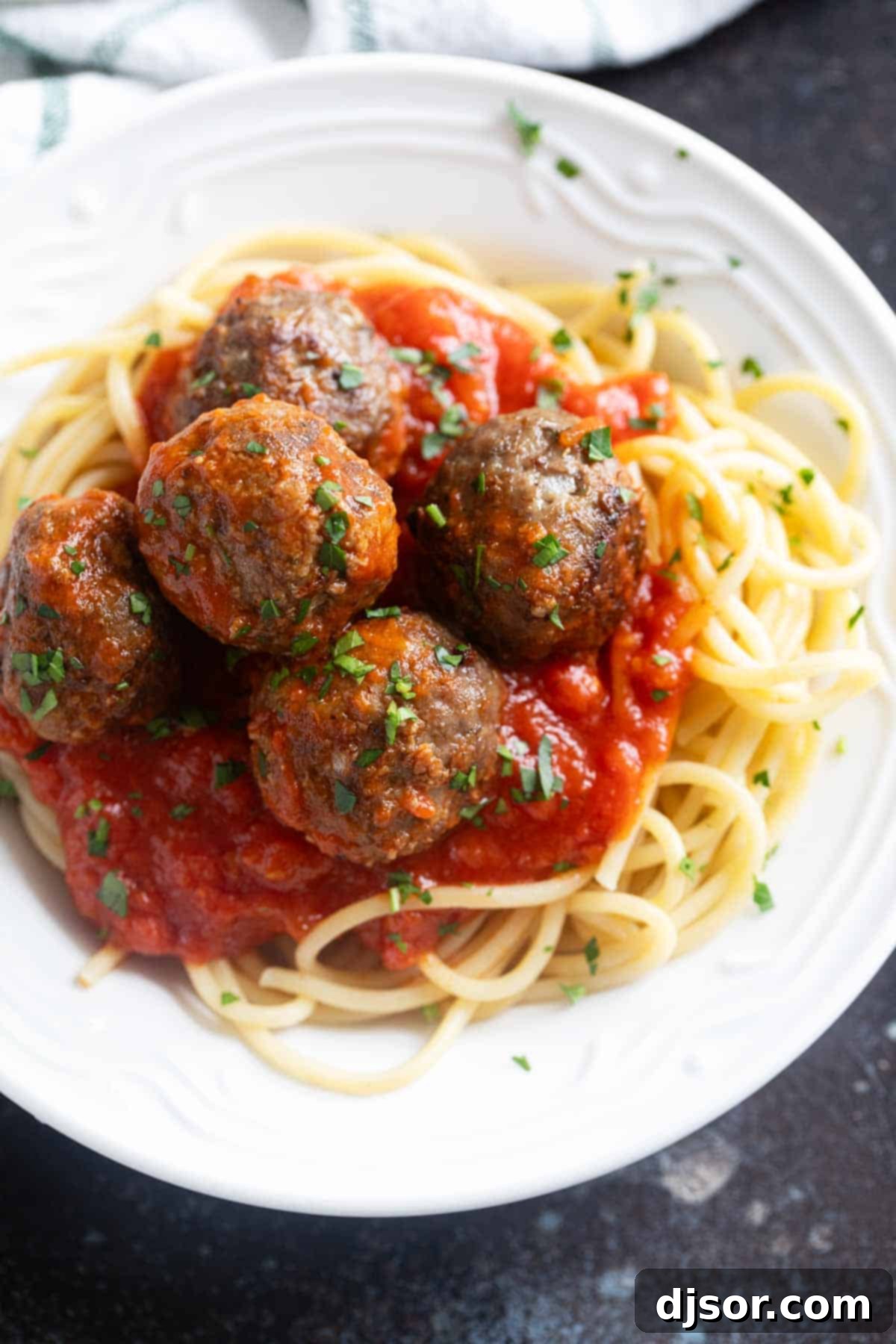 Savory Baked Meatballs 7 Close-up of baked meatballs nestled on a bed of spaghetti, generously coated in a rich tomato pasta sauce, garnished with fresh herbs and a sprinkle of Parmesan cheese.