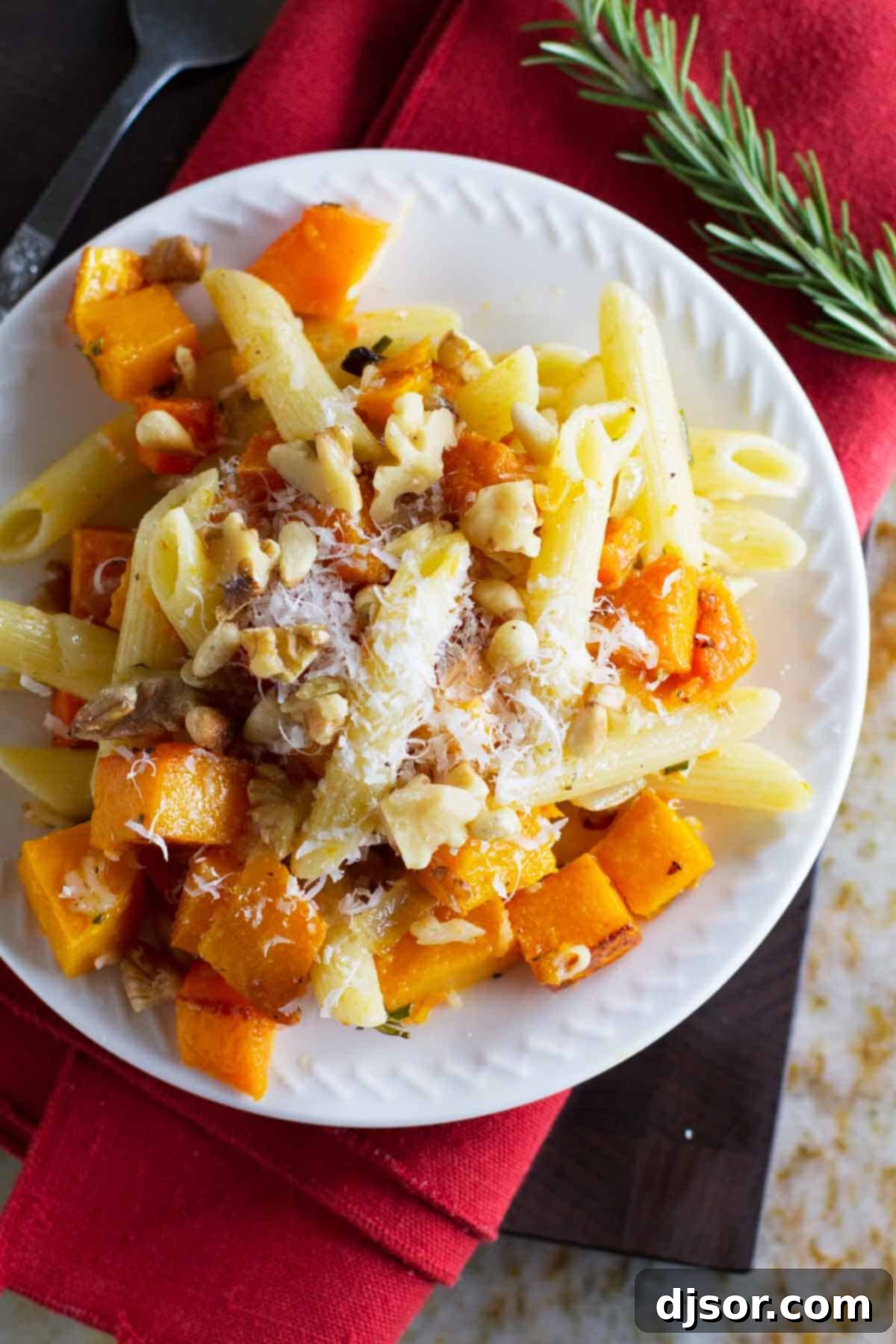 Plate filled with penne pasta, roasted butternut squash, walnuts, and rosemary.
