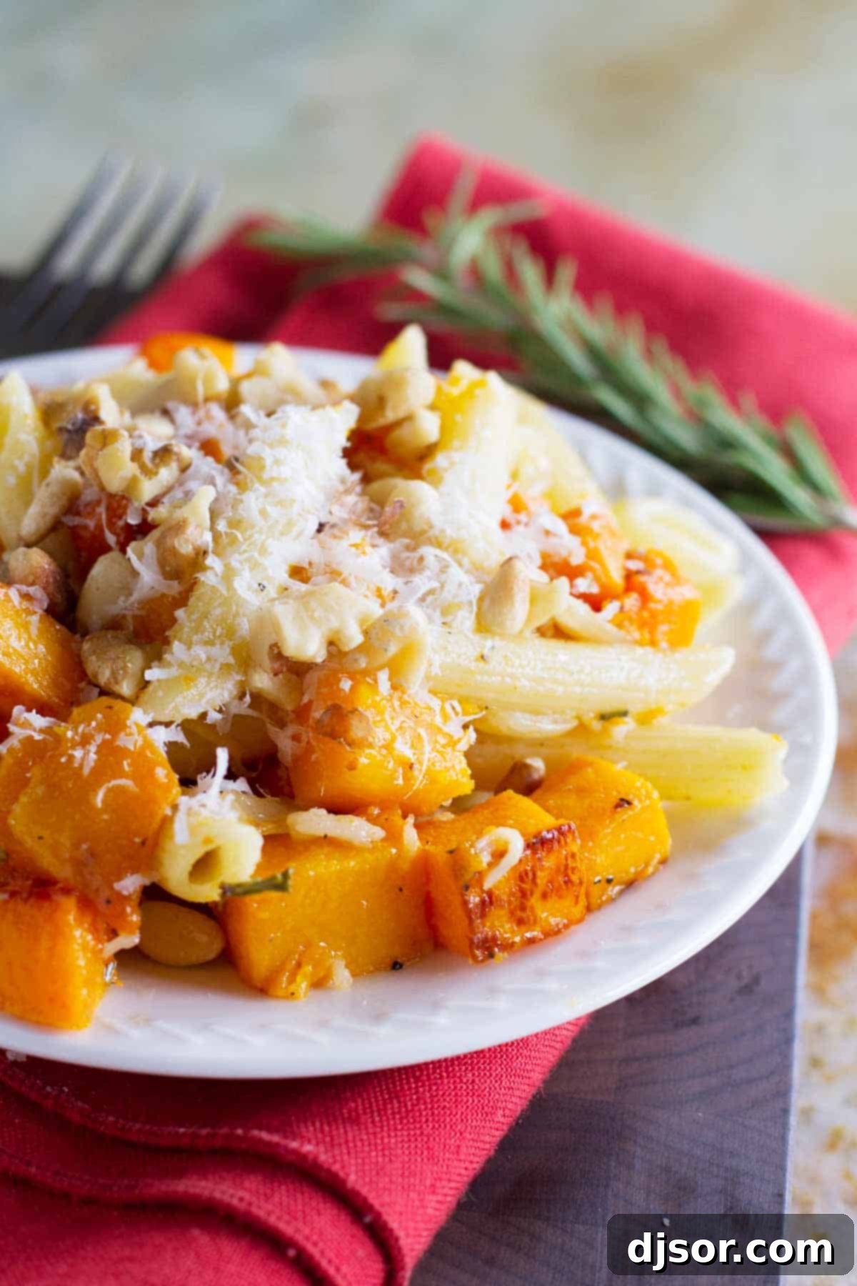 Plate filled with roasted butternut squash cubes and pasta, topped with parmesan cheese.