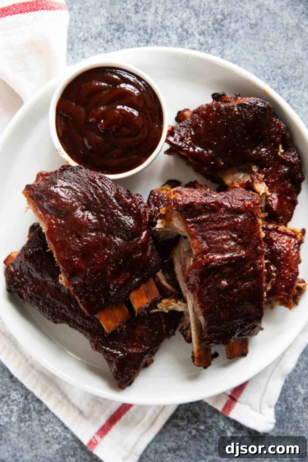 A plate brimming with sticky, tender slow cooker BBQ ribs, accompanied by a small bowl of extra barbecue sauce for dipping.