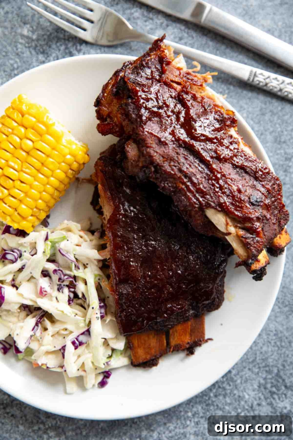 A rustic plate featuring Slow Cooker Ribs, perfectly complemented by classic side dishes of corn on the cob and creamy coleslaw.