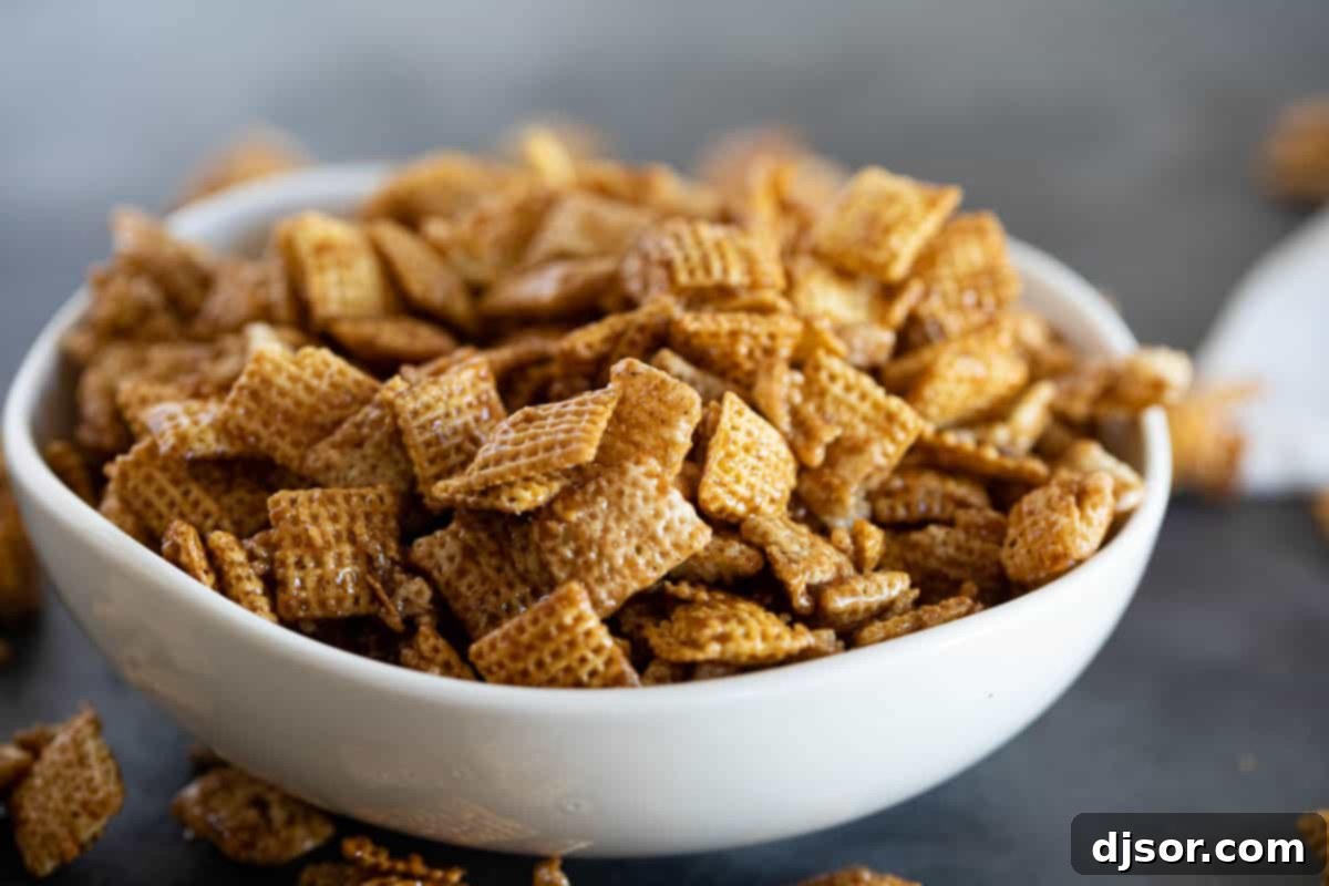 A beautifully arranged white bowl filled to the brim with golden-brown Cinnamon Caramel Snack Mix, showcasing its irresistible texture and cinnamon flecks.