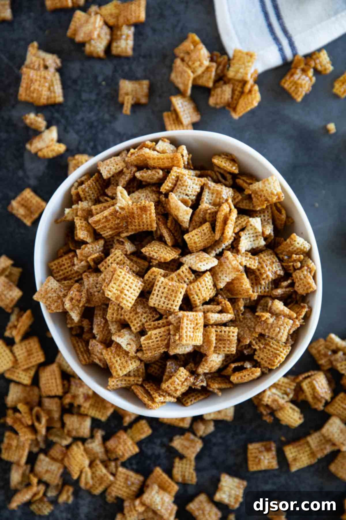 A generously filled bowl of Cinnamon Caramel Snack Mix, with extra pieces scattered enticingly around the base of the bowl, ready to be enjoyed.