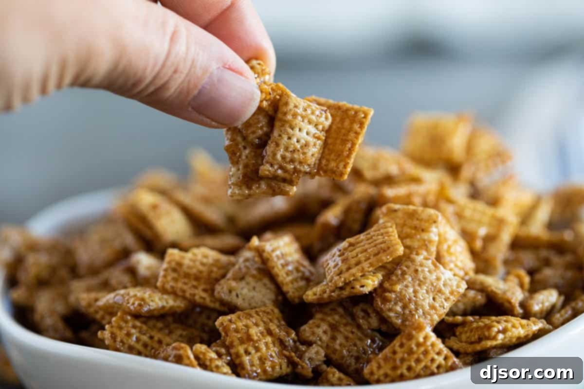 A close-up shot of fingers reaching into a bowl, eagerly picking up a handful of Cinnamon Caramel Snack Mix, emphasizing its grab-and-go appeal.