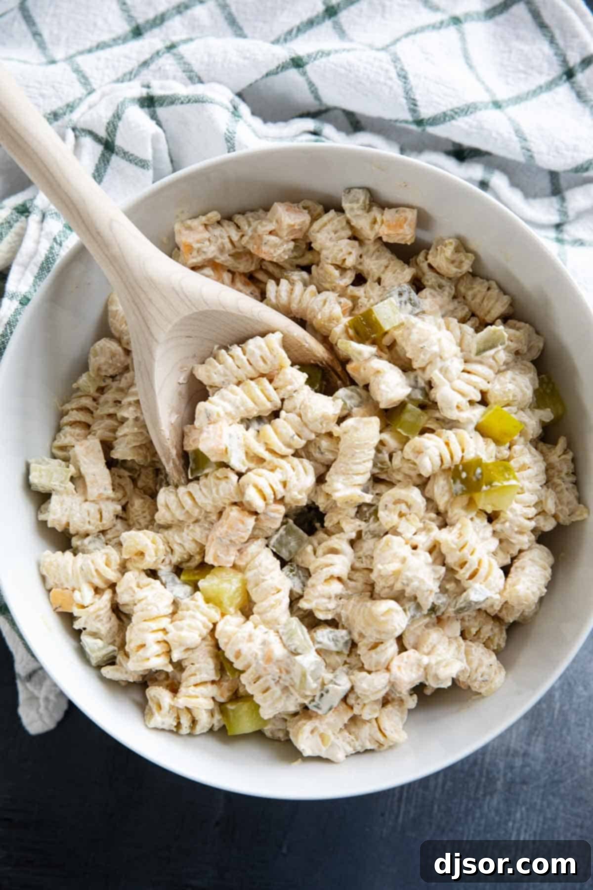 Briny Burst Pasta Salad 6 Large serving bowl filled with a vibrant Dill Pickle Pasta Salad, accompanied by a wooden serving spoon.