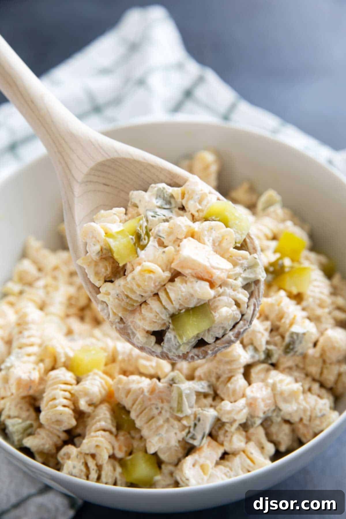 Briny Burst Pasta Salad 7 Close-up of a wooden spoon full of creamy Dill Pickle Pasta Salad, showcasing the texture and ingredients.