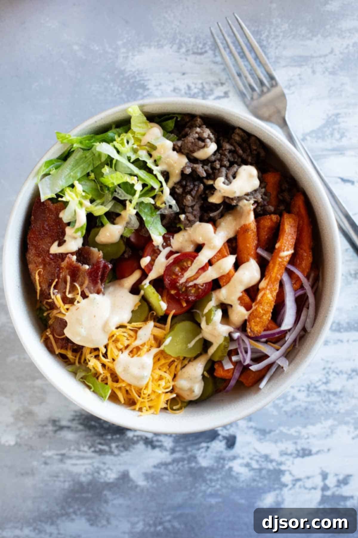 Burger Bowls with beef, sweet potato fries, onions, tomatoes, cheese, bacon, and more. A vibrant and appealing dinner option.