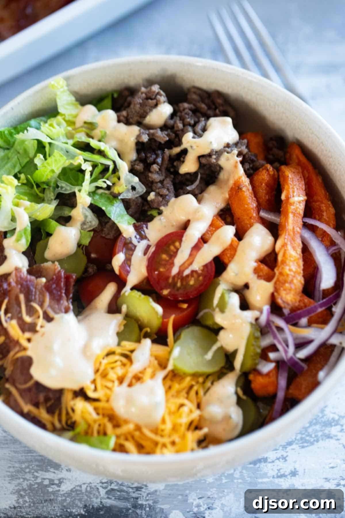 A close-up of fully assembled Burger Bowls, showcasing the sweet potato fries, ground beef, toppings, and special sauce, ready to be enjoyed.