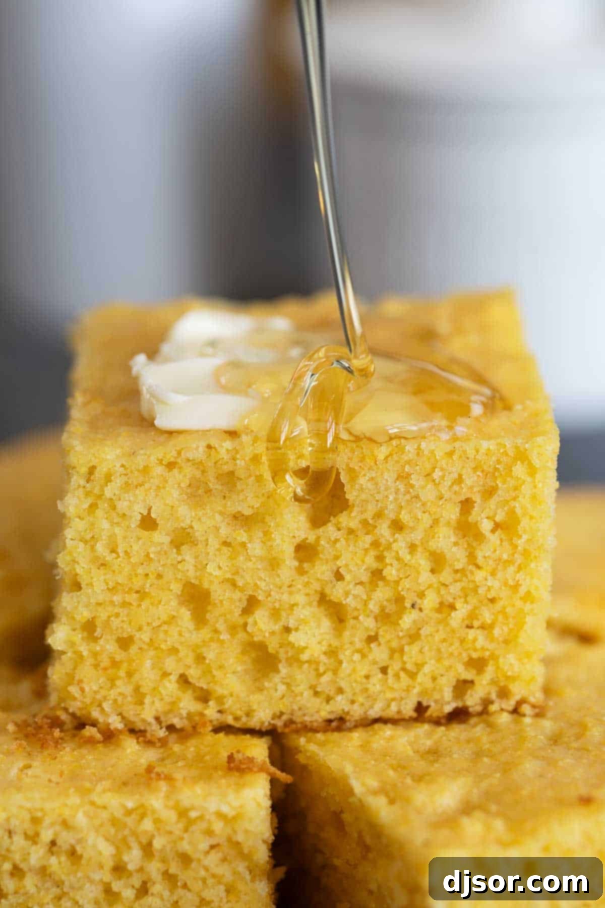 Honey being drizzled generously over a warm slice of Sour Cream Cornbread.