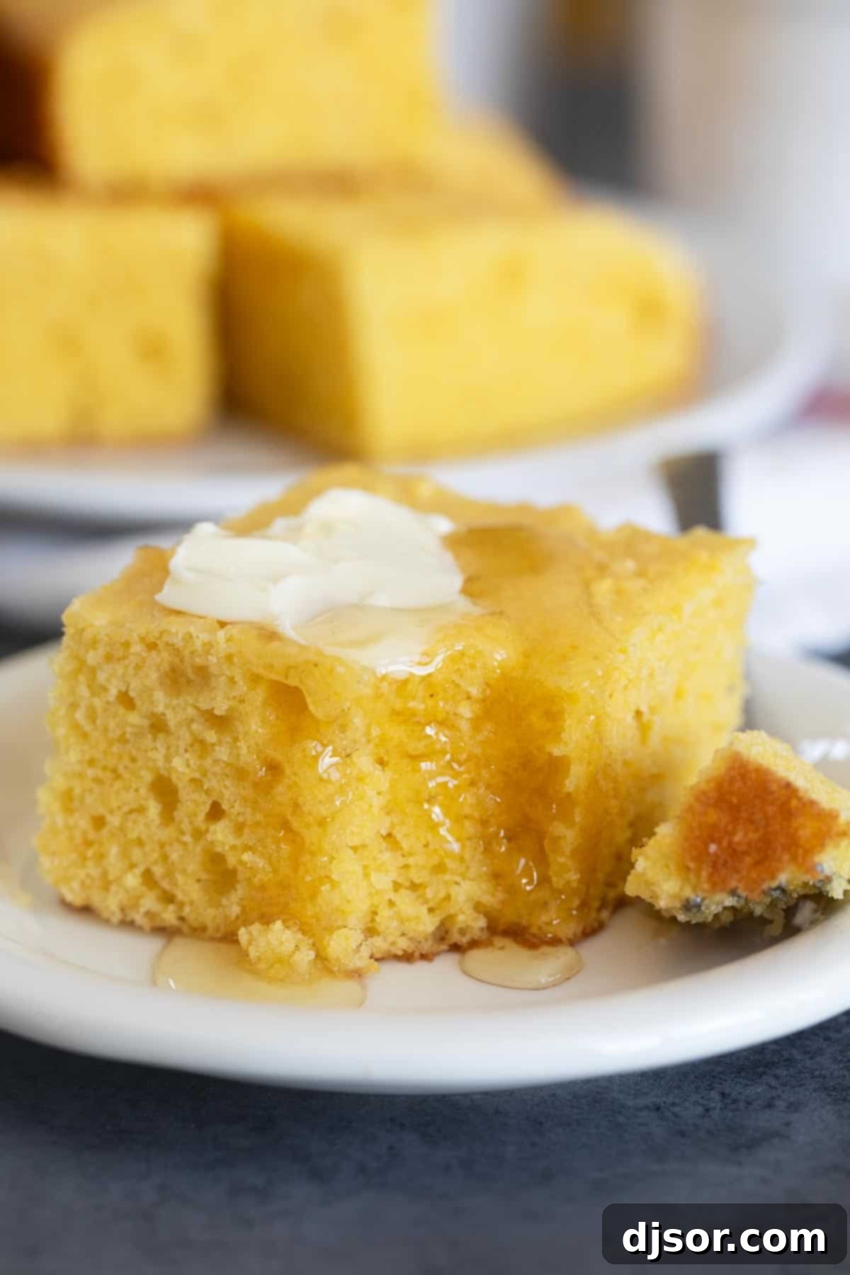 A delectable slice of sour cream cornbread, buttered and drizzled with honey, with a bite taken.