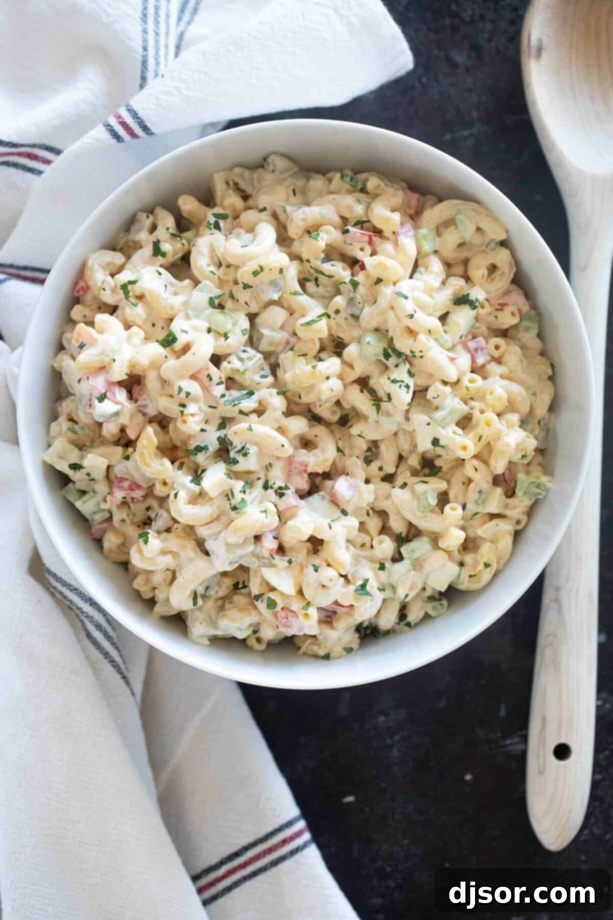 Creamy Macaroni Delight 6 A beautifully presented bowl of creamy macaroni salad, garnished and ready to serve with a wooden spoon.