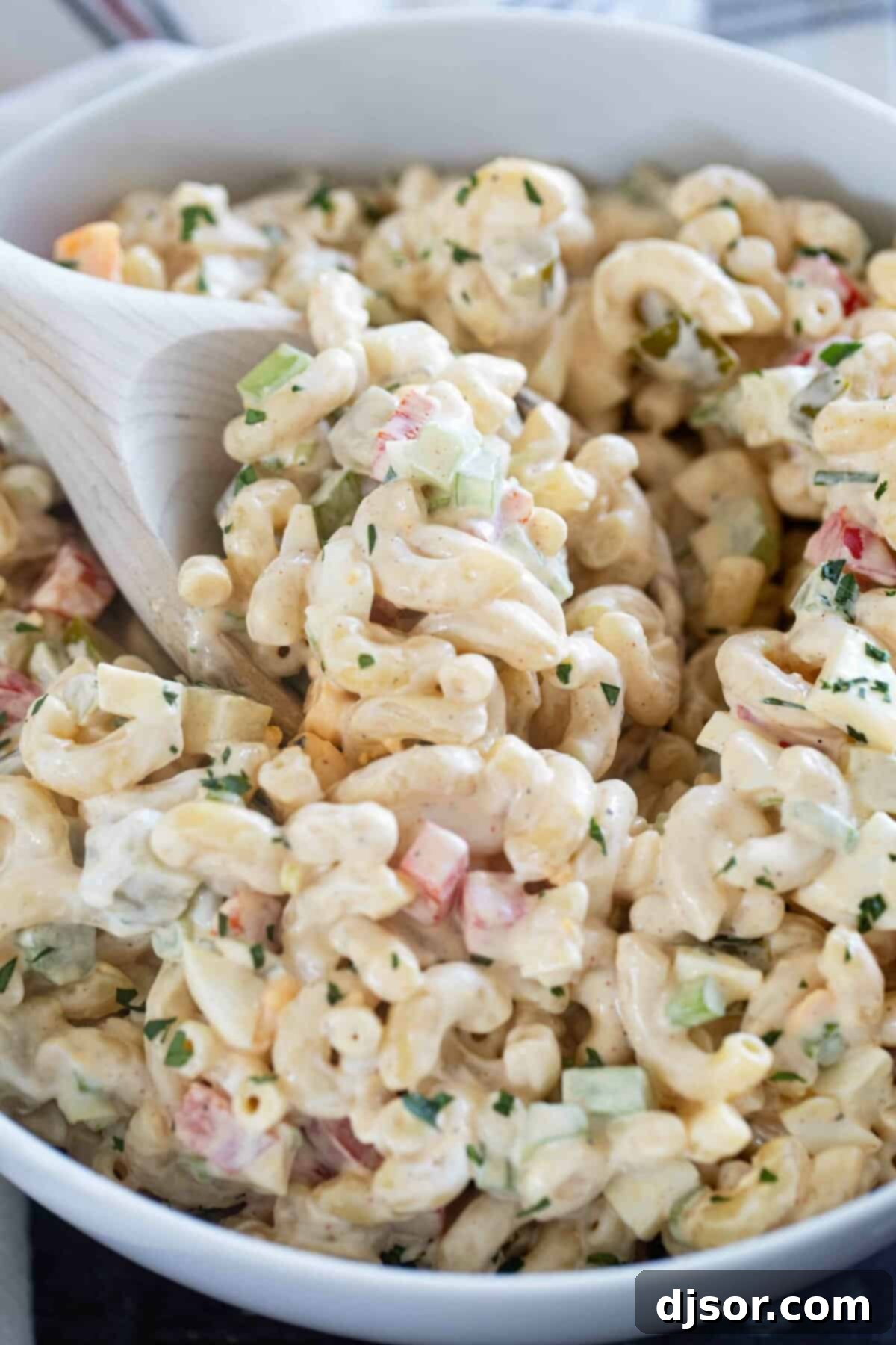 Creamy Macaroni Delight 7 A bowl of creamy macaroni salad with a wooden serving spoon, ready to be enjoyed.
