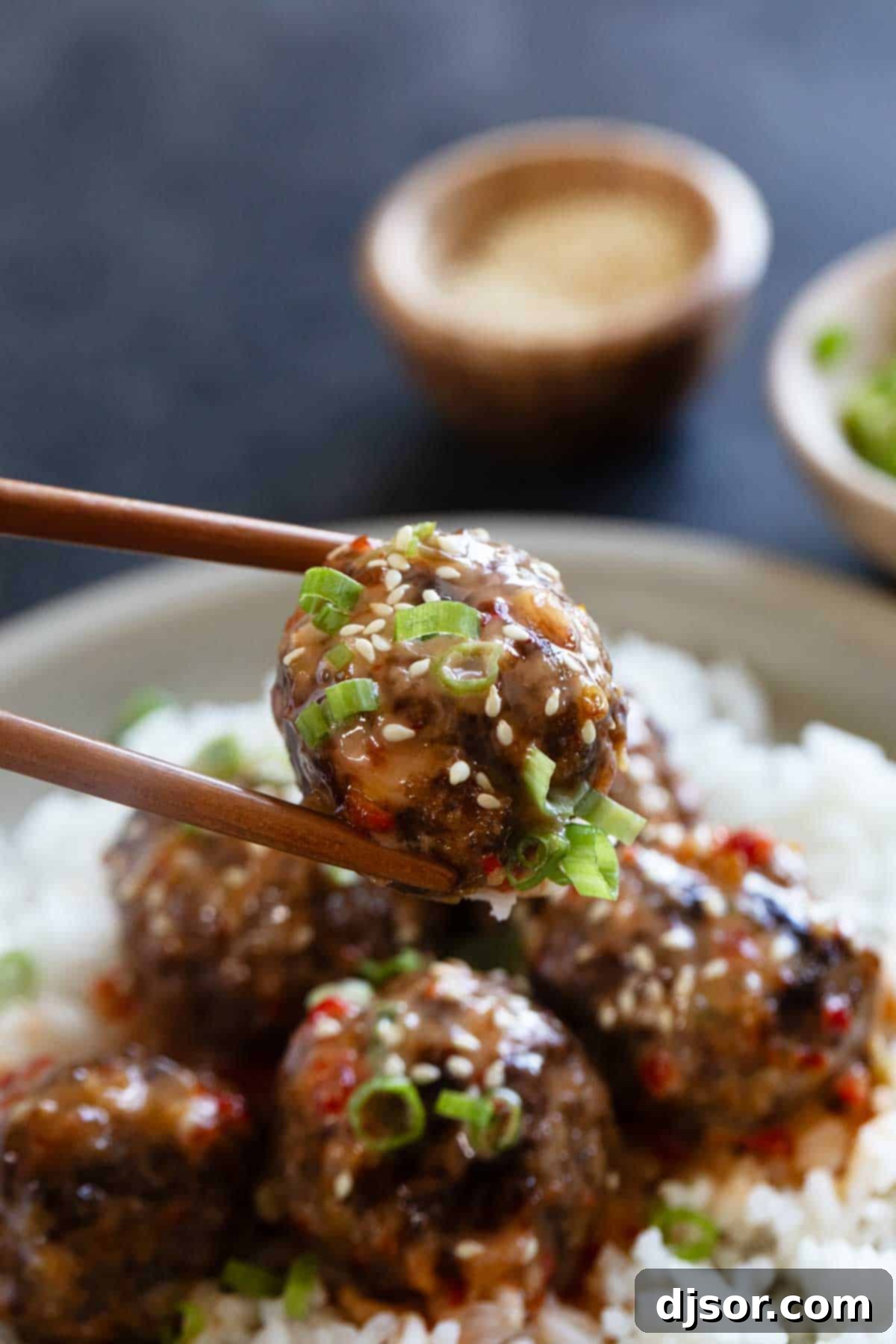 Firecracker Meatballs on a plate with one meatball being held by chopsticks.