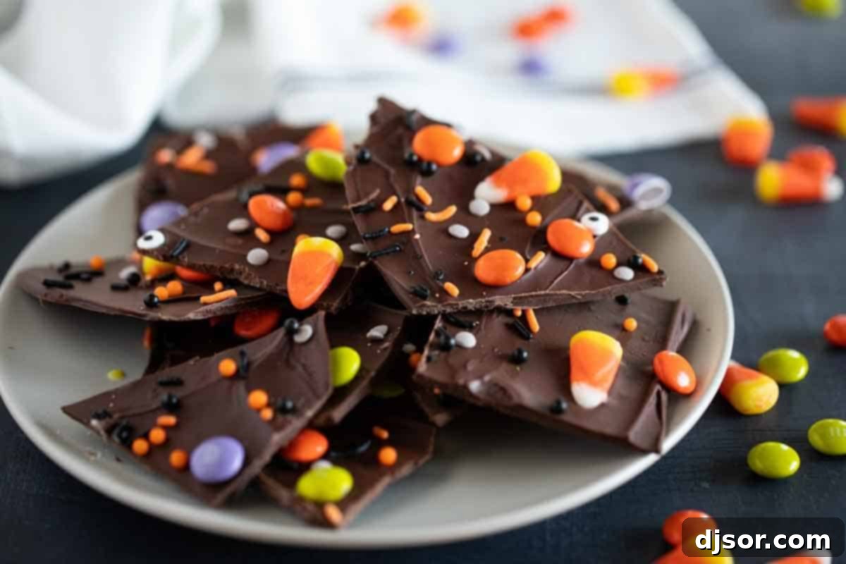 Plate with pieces of Halloween candy bark, topped with various Halloween candies like candy corn, M&Ms, and sprinkles with edible eyeballs.