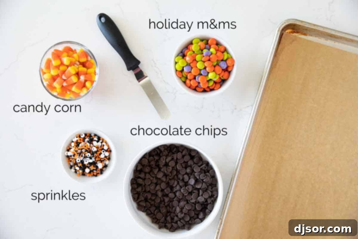 Ingredients to make Halloween Candy Bark laid out on a table: chocolate chips, candy corn, Halloween-colored M&Ms, and sprinkles with edible eyeballs.