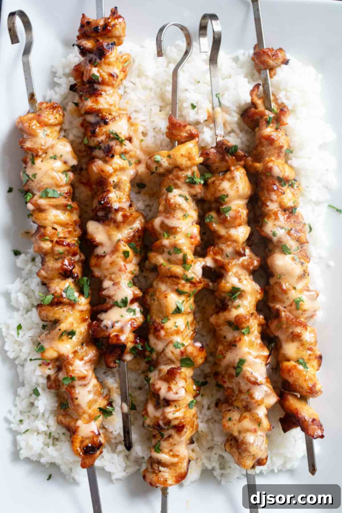 Ultimate Bang Bang Chicken Skewers 2 Bang Bang Chicken Skewers over rice on a platter, garnished with fresh cilantro.