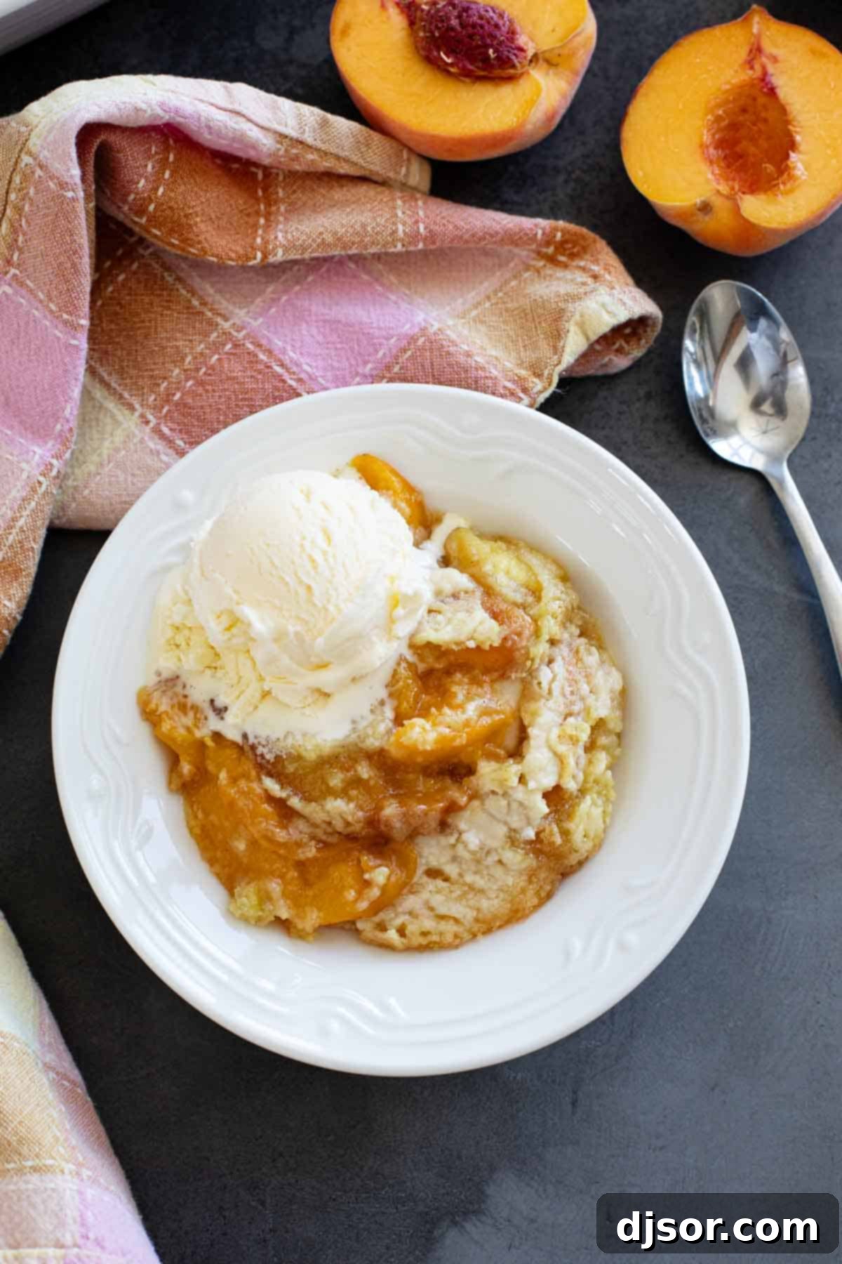 A serving of warm peach dump cake, topped with a scoop of creamy vanilla ice cream, in a white bowl.