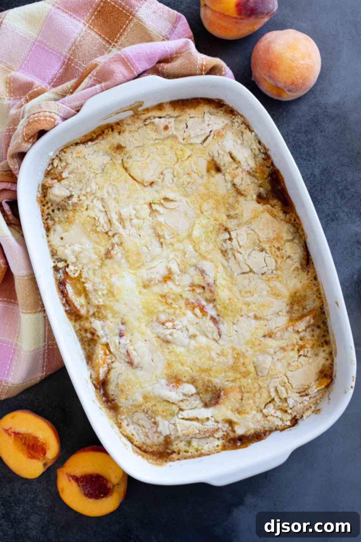 A freshly baked peach dump cake, still in its baking dish, with vibrant fresh peaches scattered around it.