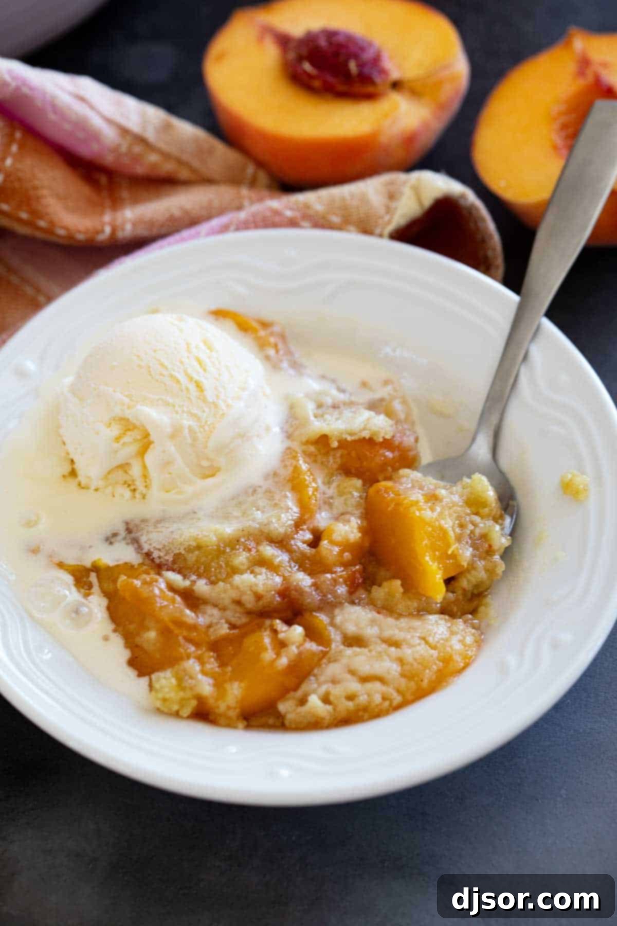 A close-up shot of a bowl of warm peach dump cake, generously topped with a scoop of melting vanilla ice cream.