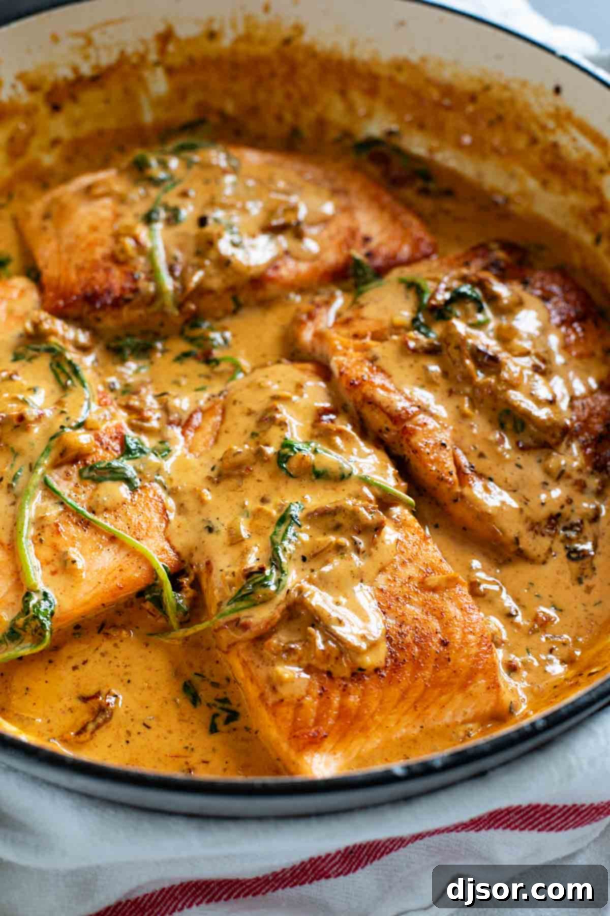 Tuscan Salmon simmering in a skillet with a vibrant sun-dried tomato cream sauce and fresh spinach.