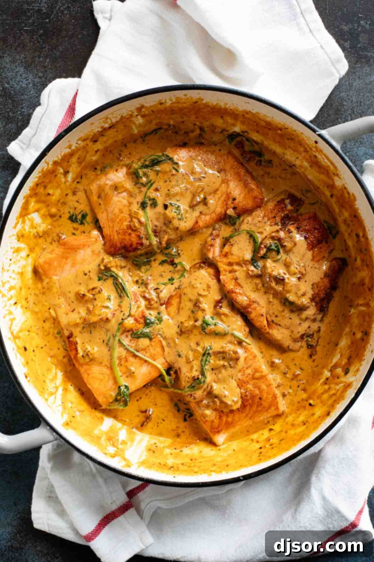 A large skillet filled with perfectly cooked Tuscan Salmon, bathed in creamy sun-dried tomato and spinach sauce, ready to serve.