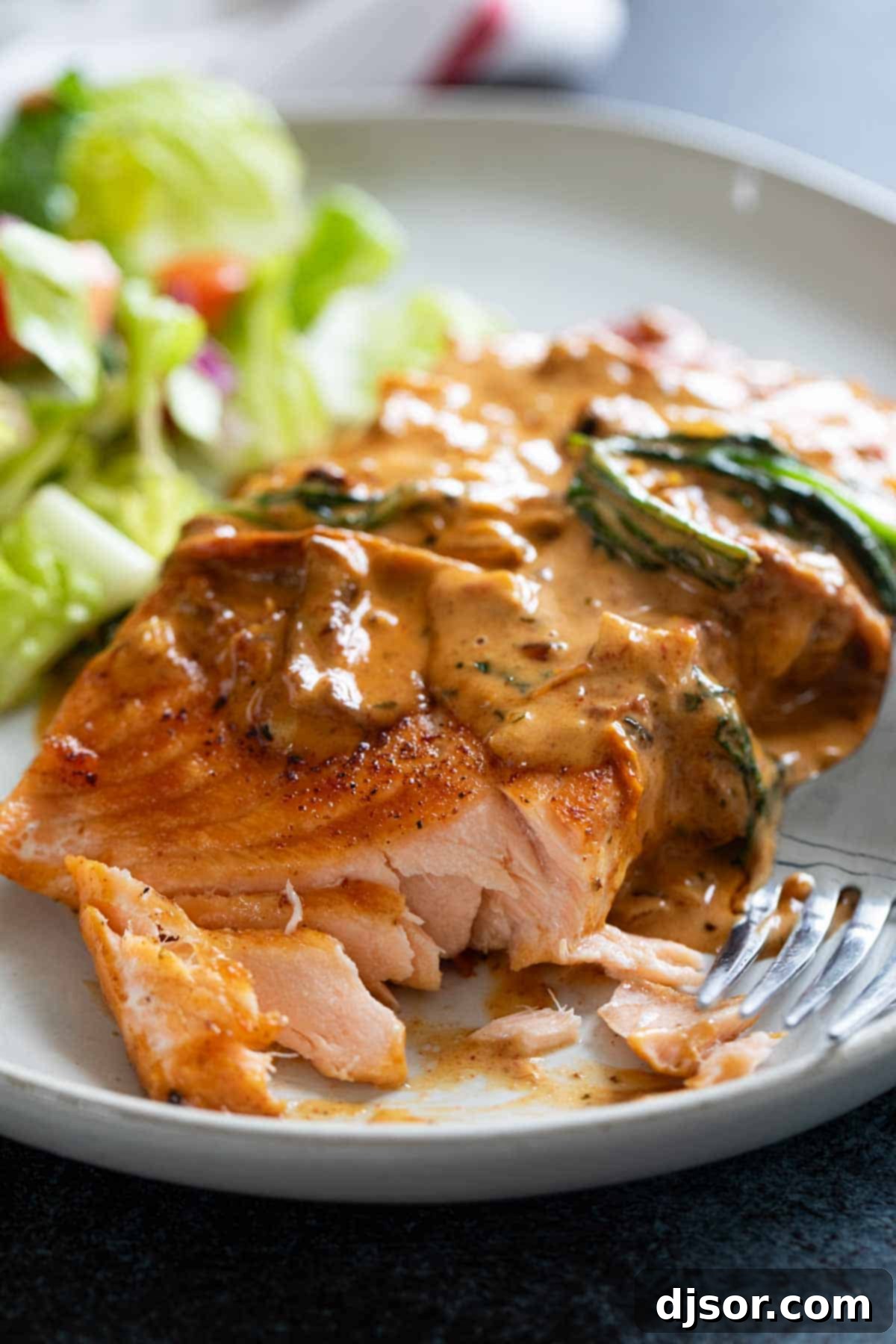 A serving of Tuscan Salmon on a white plate, with a bite taken, showcasing the flaky fish and creamy sauce.