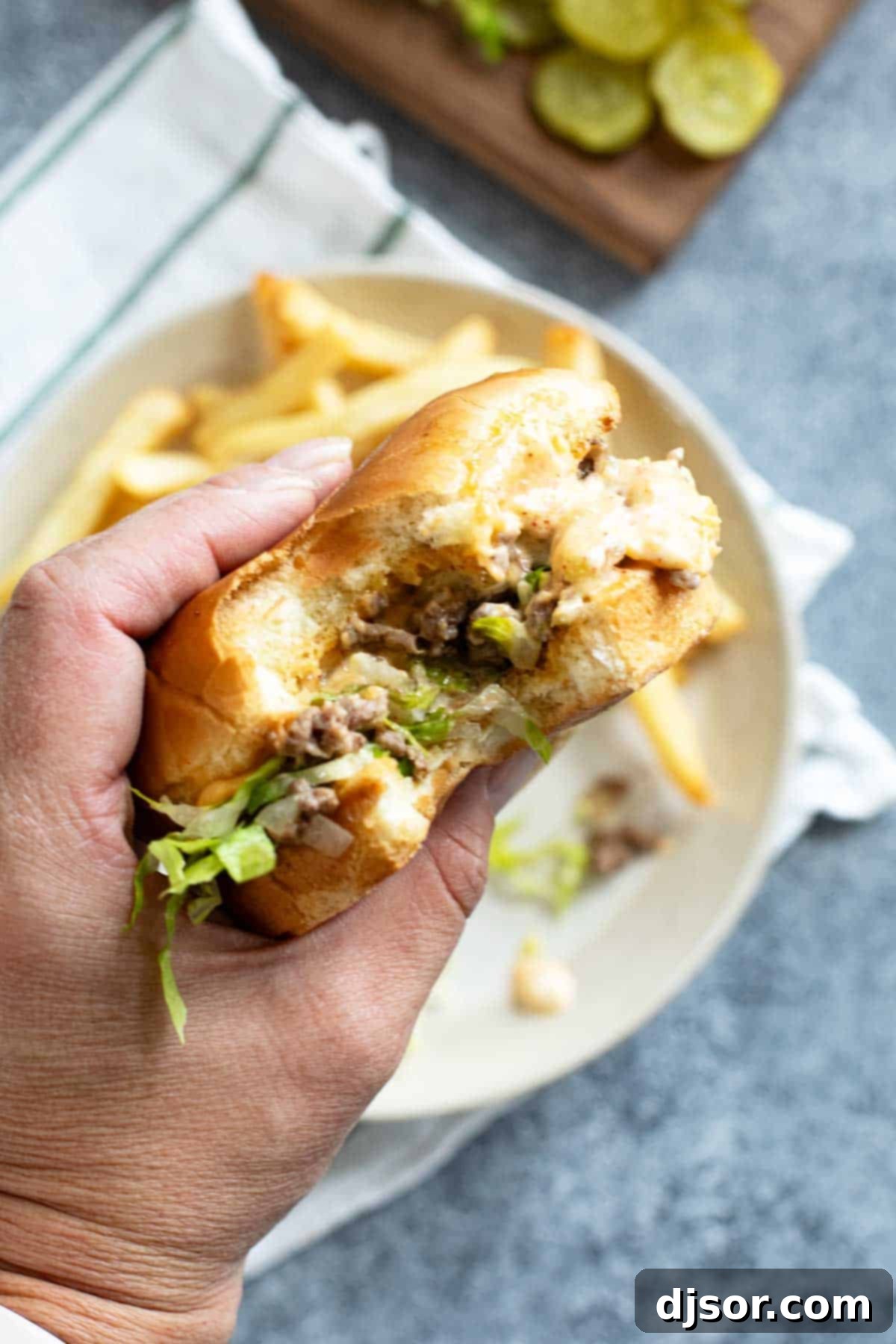 Hand holding a Big Mac Sloppy Joe with a bite taken from it.