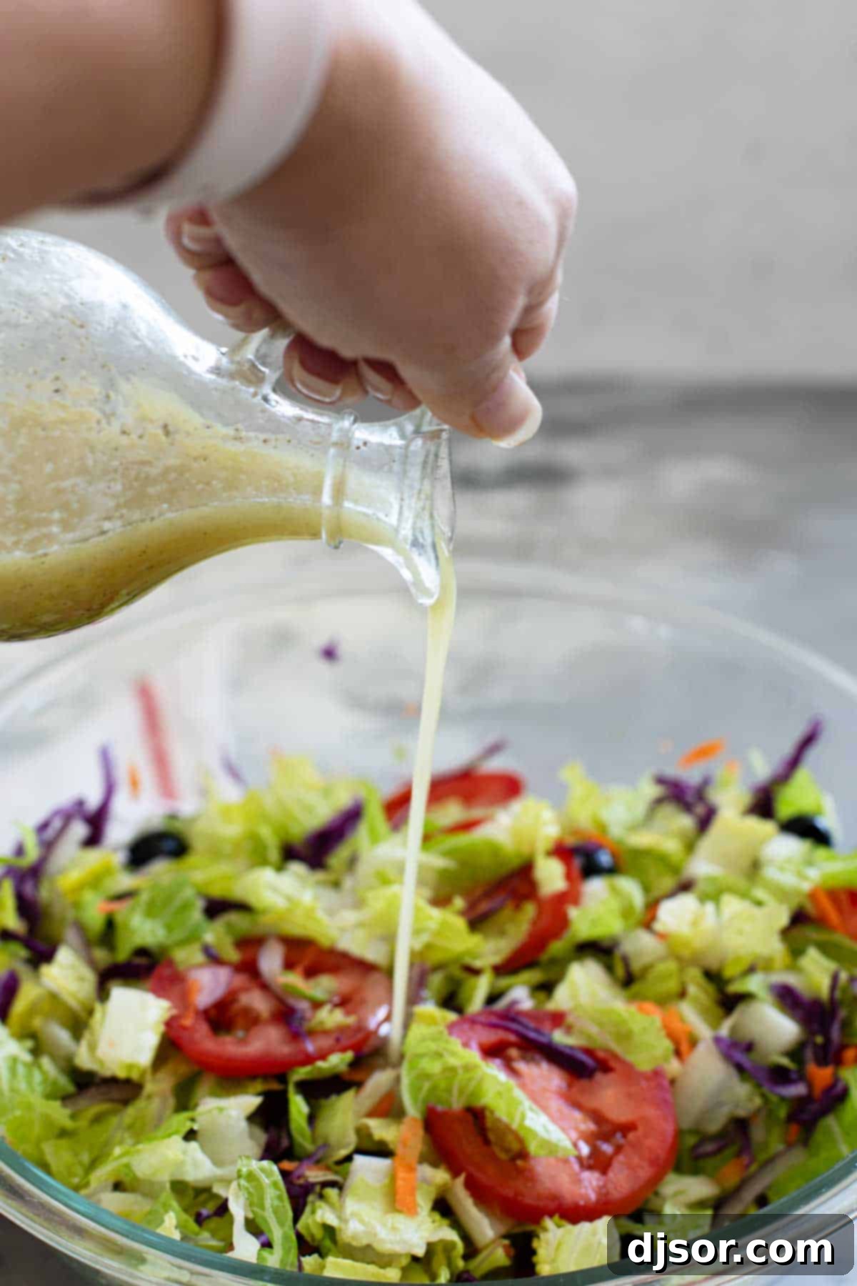 Delicious Olive Garden copycat dressing being poured over a fresh, vibrant green salad in a white bowl, garnished with croutons.