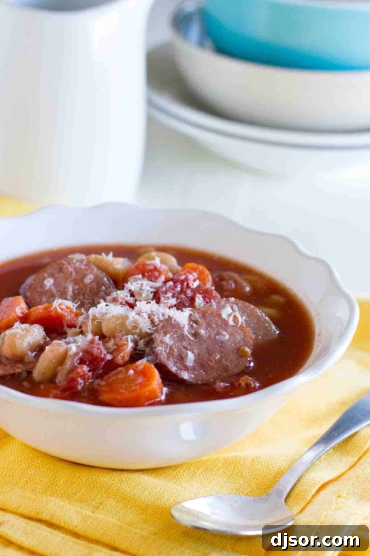 Bowl of slow cooker white bean soup with sausage on a yellow napkin.