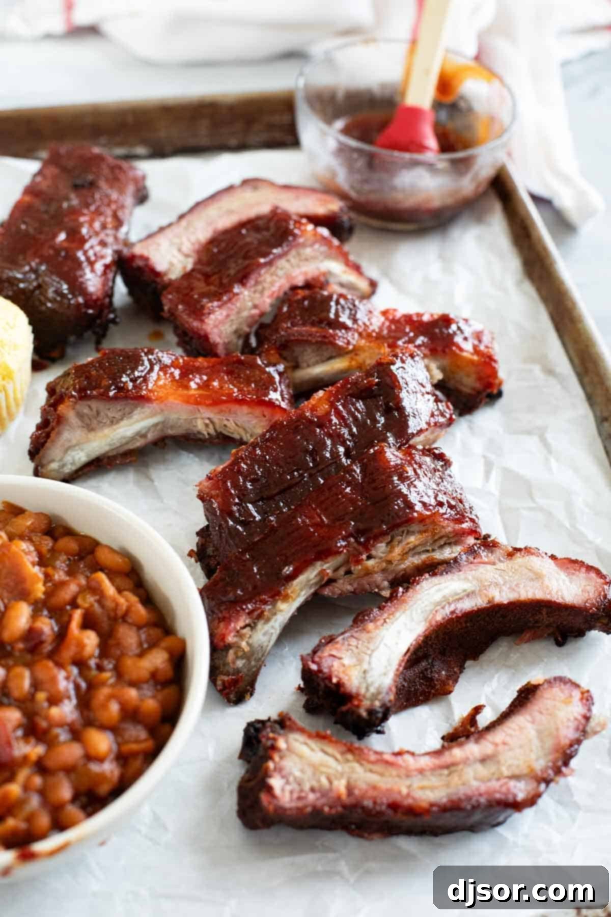 Slow-Smoked Ribs 2 Smoked ribs on a tray with baked beans and corn muffins, ready to be served.