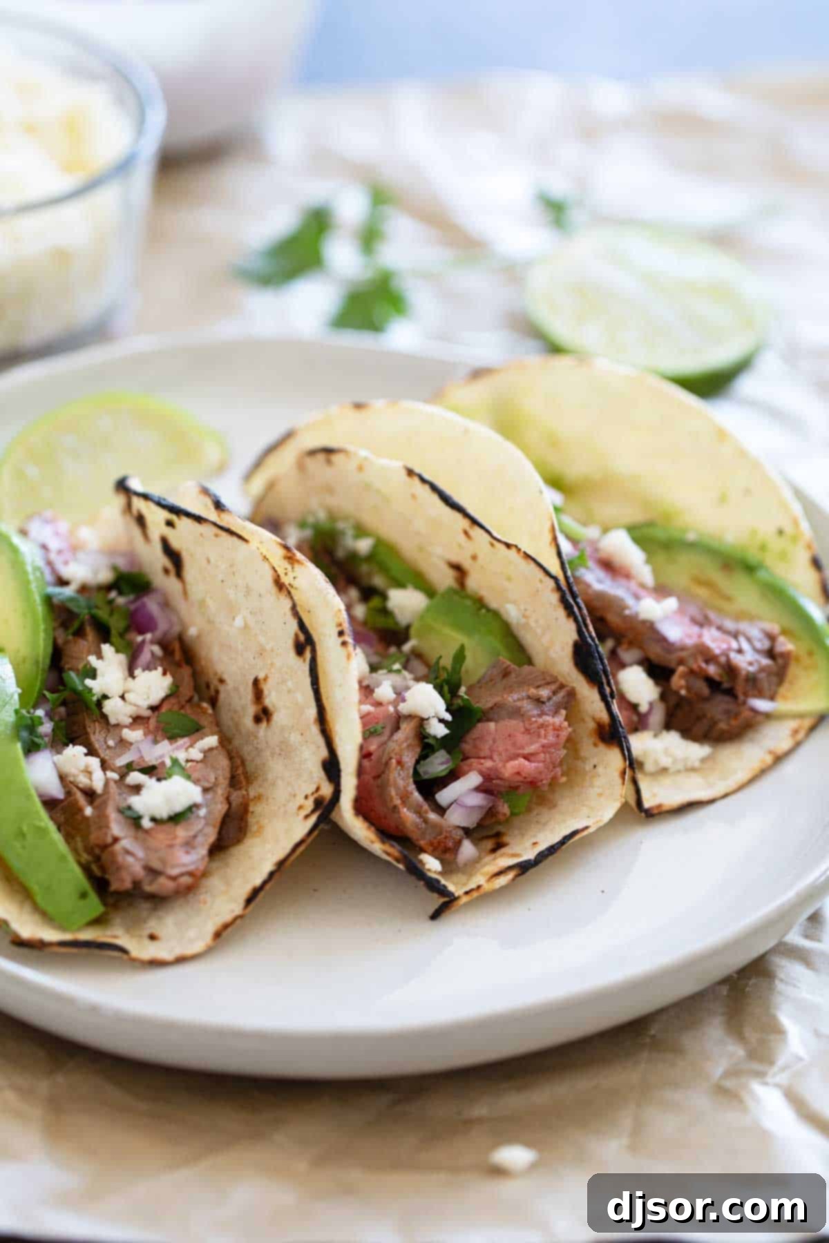 Street Style Flank Steak Tacos 2 Flank Steak Tacos on corn tortillas on a plate, garnished with fresh cilantro and red onion.