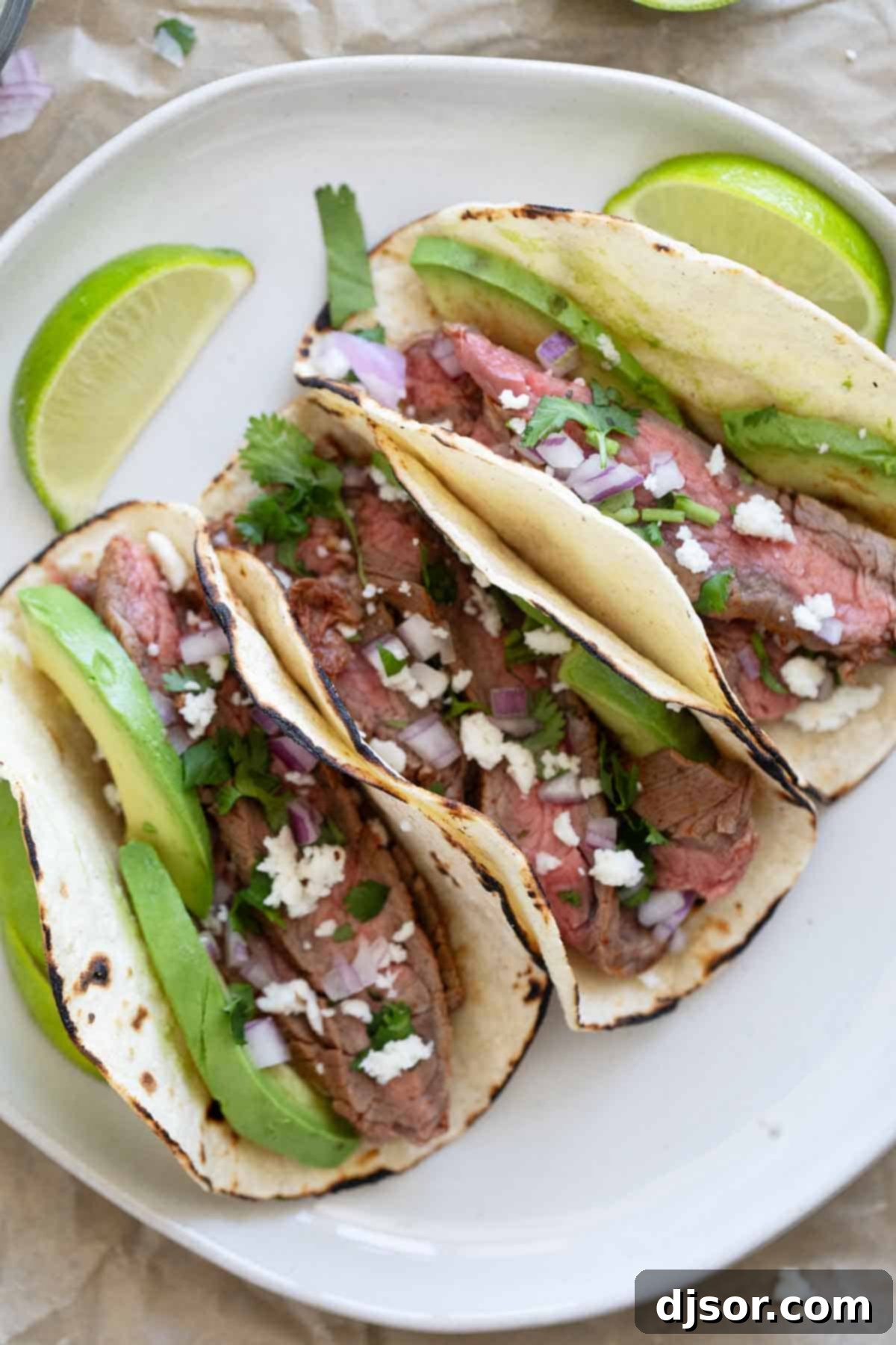 Street Style Flank Steak Tacos 7 Three flank steak tacos arranged on a plate, showcasing the sliced steak and various toppings.